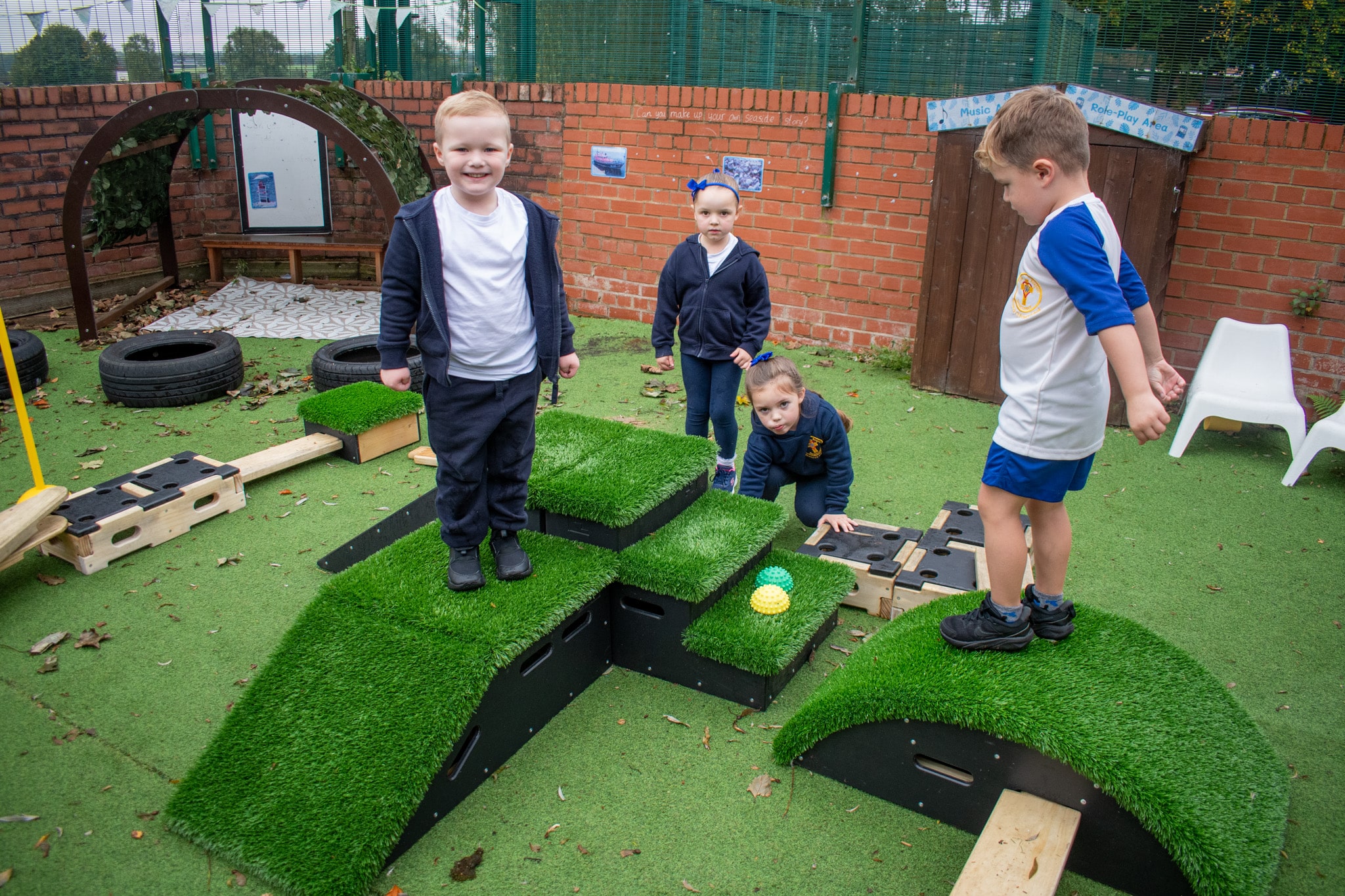 4 children are climbing on the freestanding active play equipment as they explore their new environment. Once child is looking into the camera and is smiling.