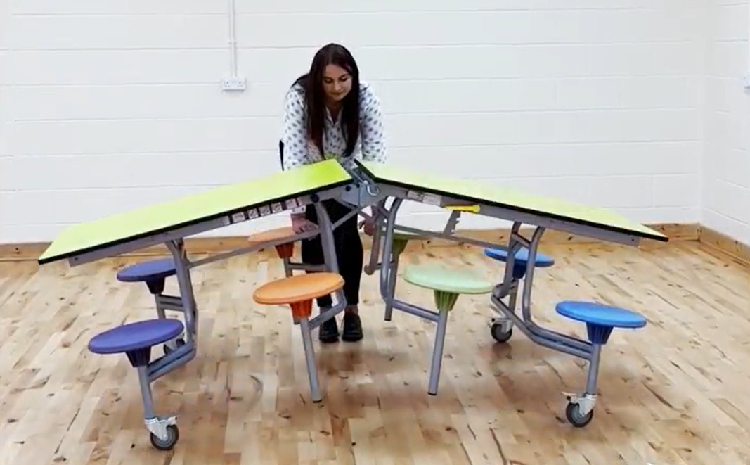 A woman is unfolding a school dining table, showcasing how easy it is to manoeuvre them.