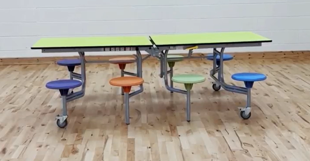 An unfolded school dining table with 8 seats. The table has a green top and different coloured stools.