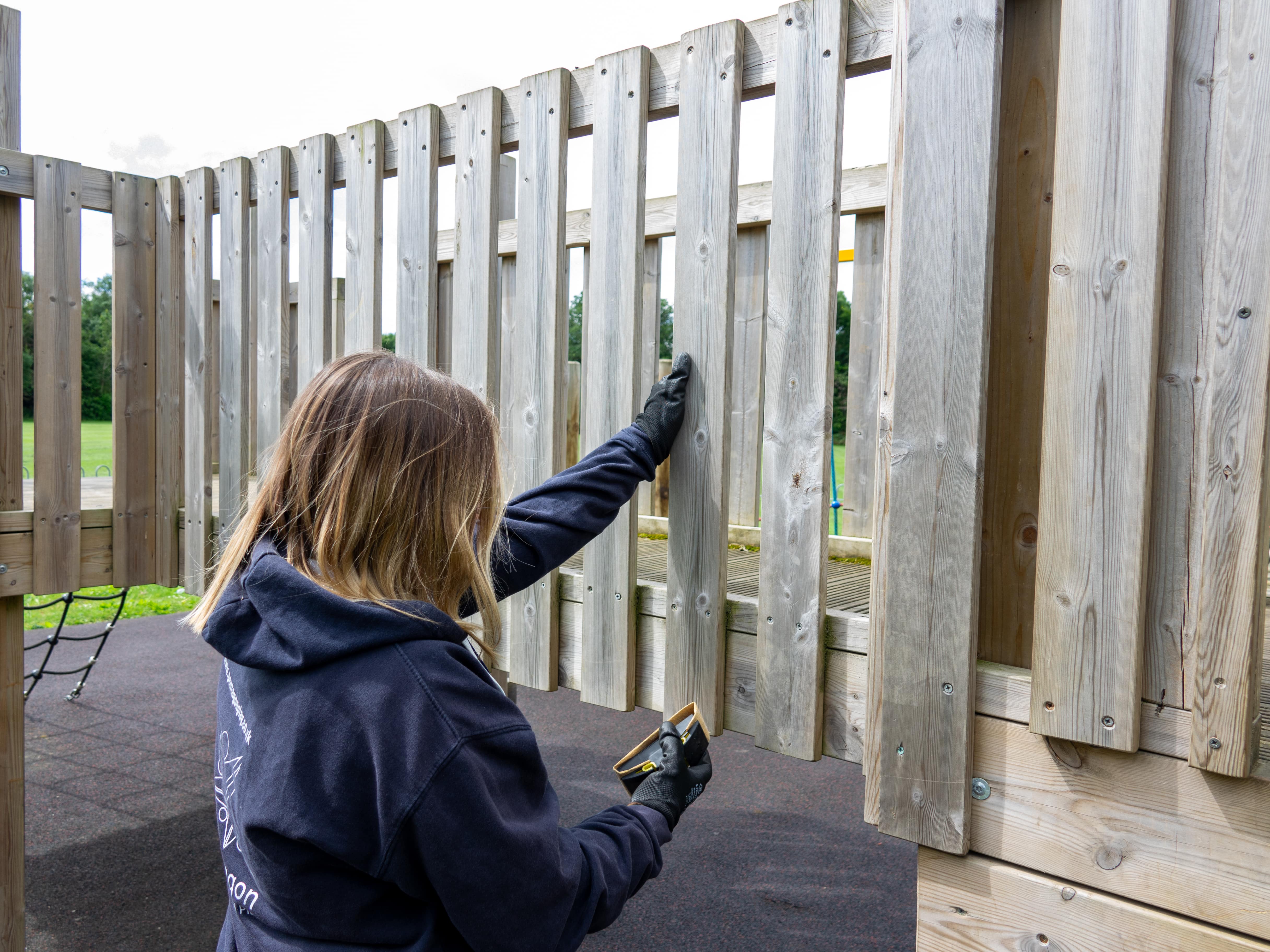 A playground inspector is looking at wooden fence panels and is using a tool to look for any structural weakness or damage.