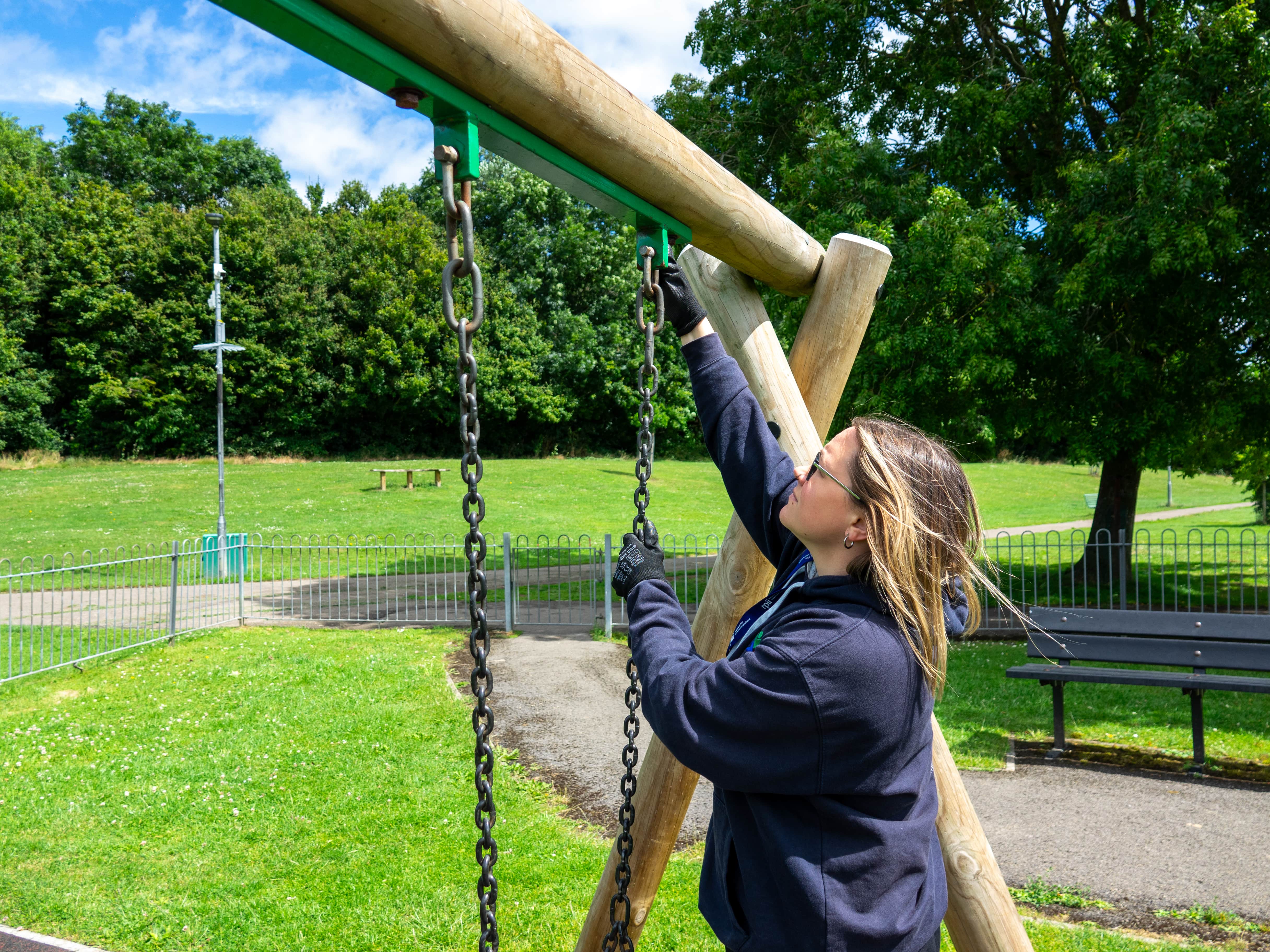 A playground inspector is looking at the strength of a swing chain and is pulling certain parts of it.