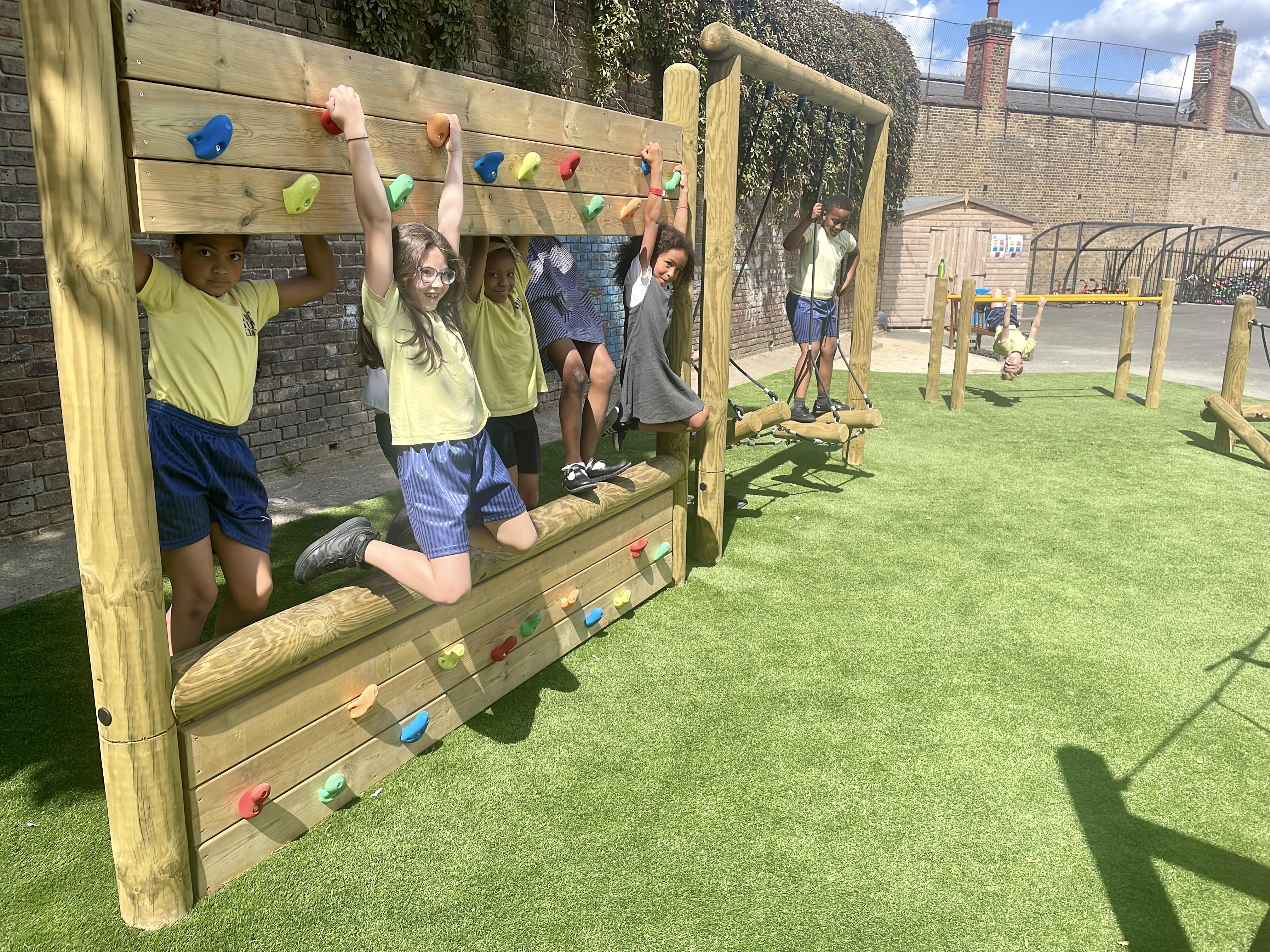 A few children are climbing on the double sided climbing wall and are looking into the camera.