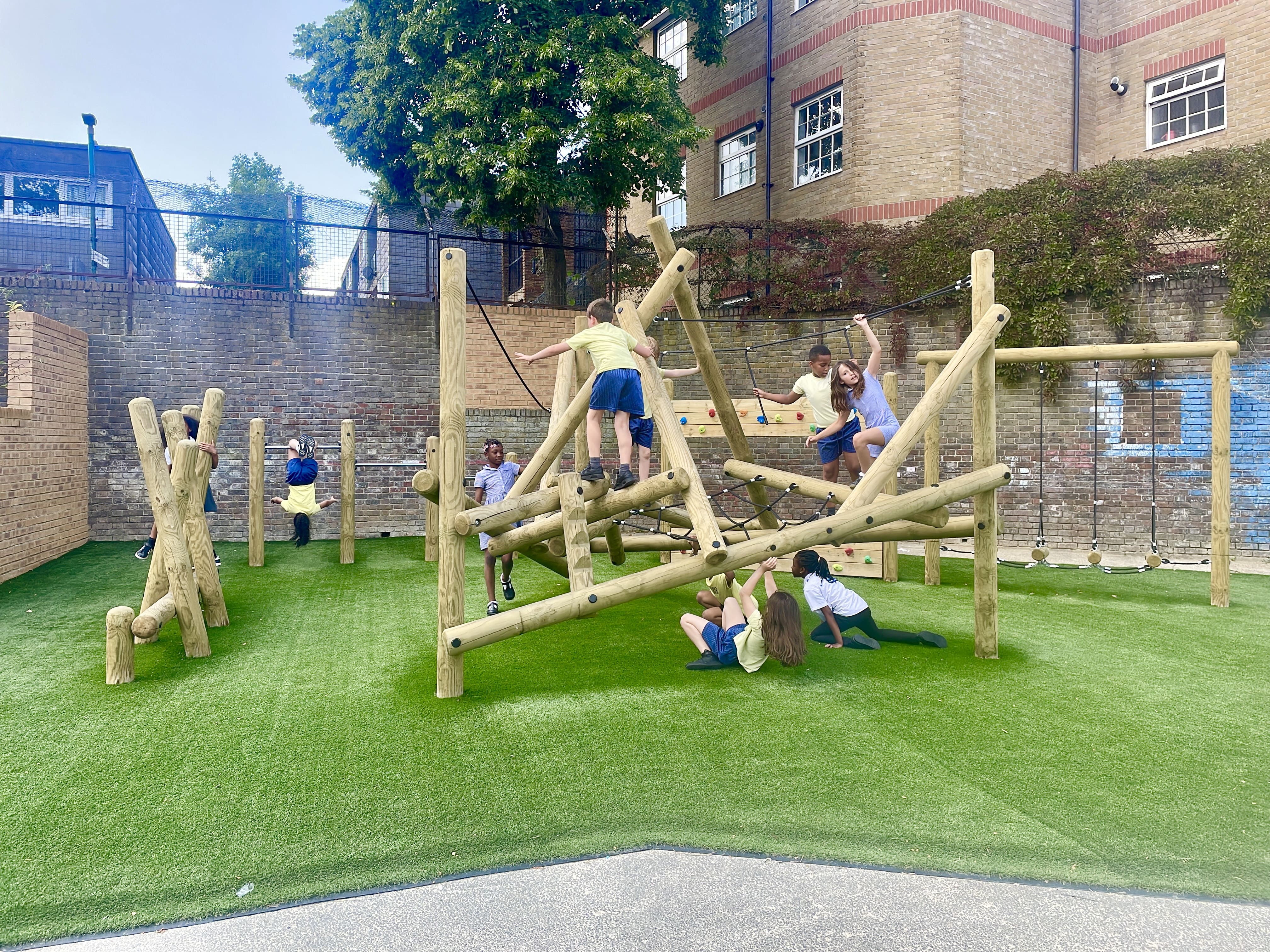 A trim trail and a Bowfell Climber have been installed on top of Playturf artificial grass. A group of children are playing with the equipment.