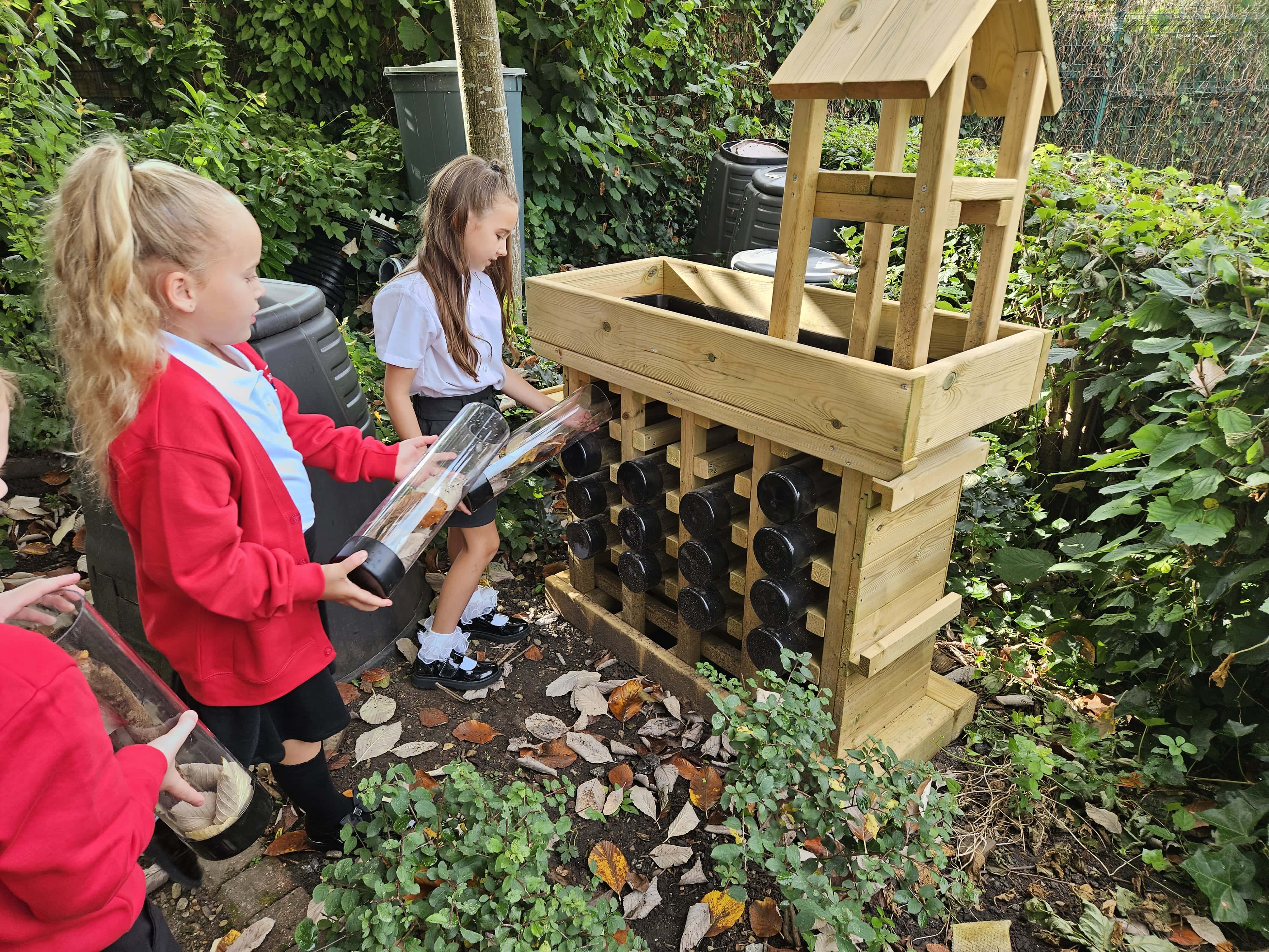 A few children are engaging with the bug hotel and are taking the pods out the bug hotel. The children look engaged with the activity.