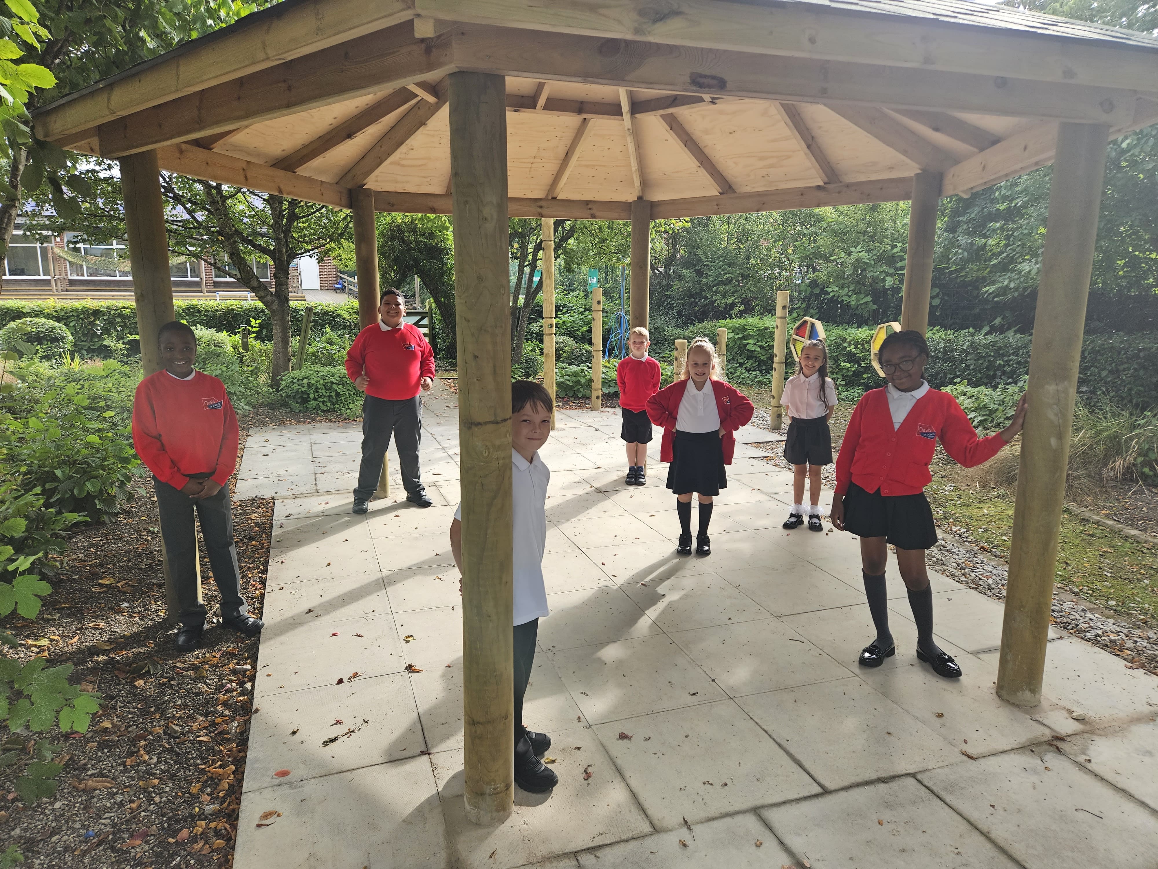 A large group of children are stood underneath a 5M gazebo and are all looking towards the camera and are smiling.