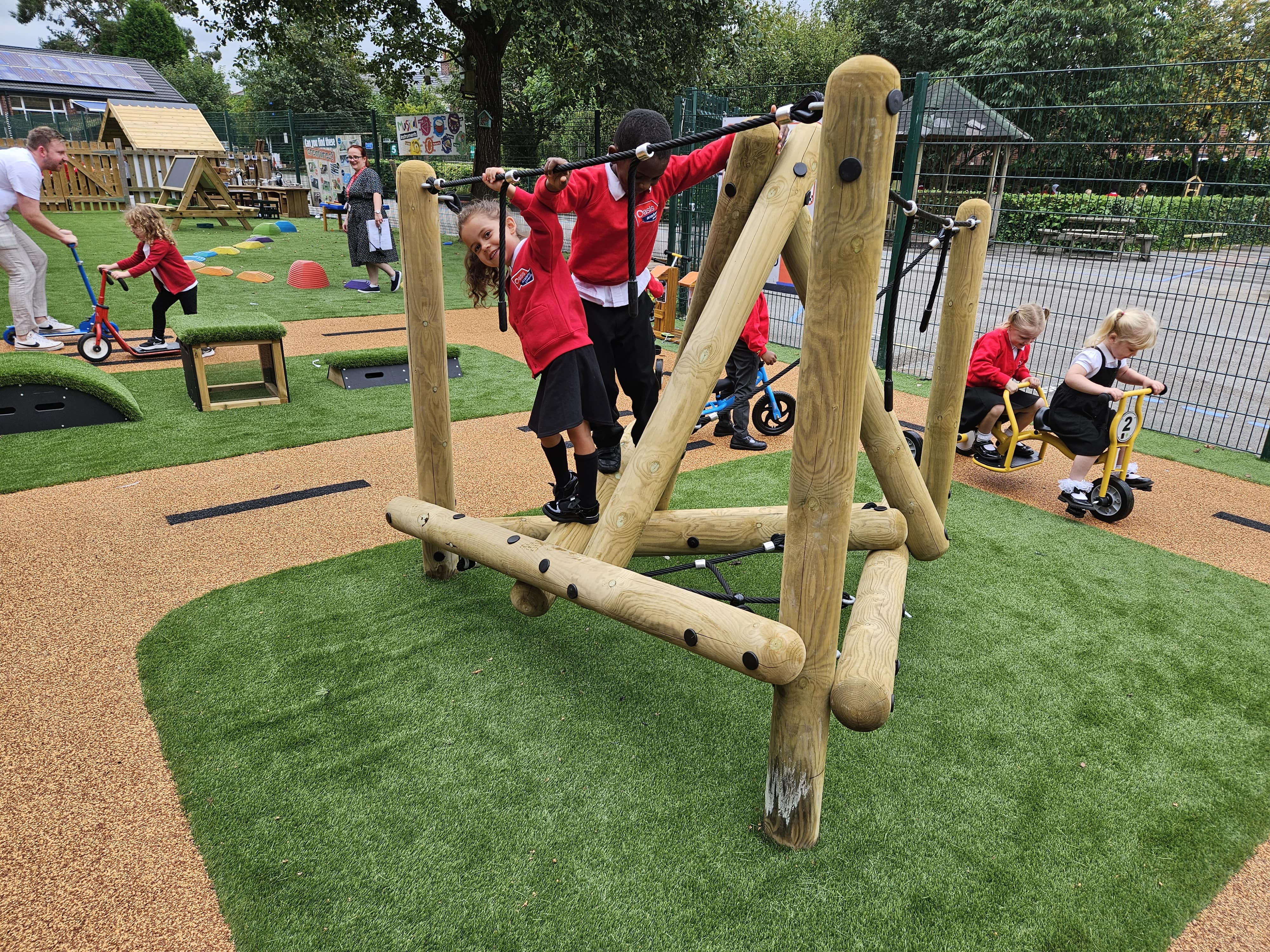 A few children are exploring a climbing frame, whilst children in the background are playing on tricycles and scooters.