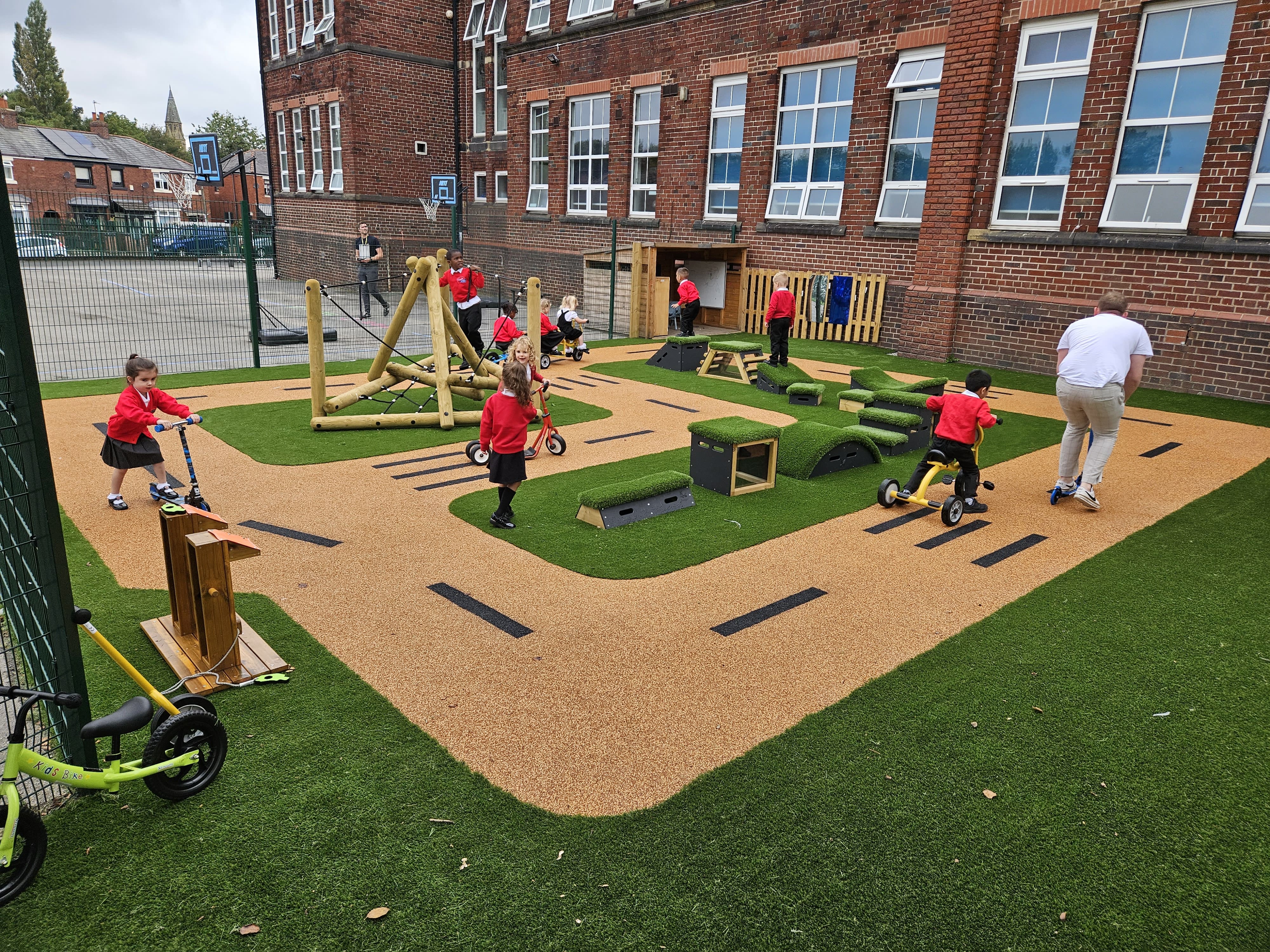 An EYFS play area that has a group of children playing on it. A variety of freestanding play equipment can be seen, in addition to tricycles and a climbing frame.