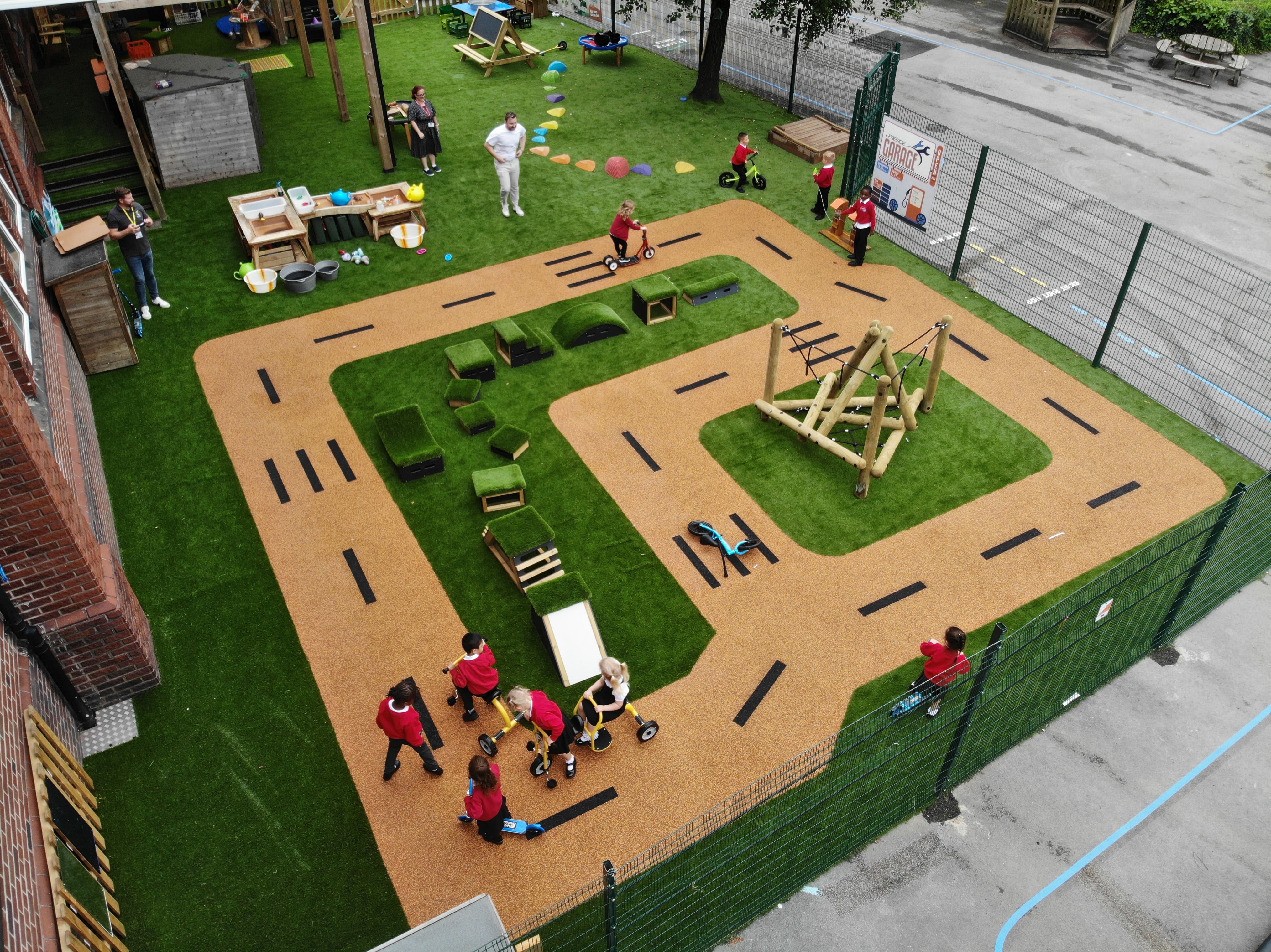 A birds eye view of the EYFS play area, showcasing the wetpour and artificial grass surfacing. A group of children are playing on the surface and are engaging with freestanding play equipment.