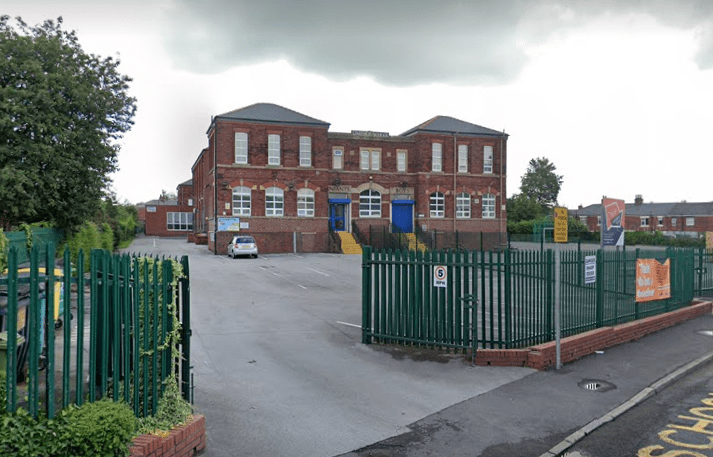 An brick-built school with green gates and a big driveway