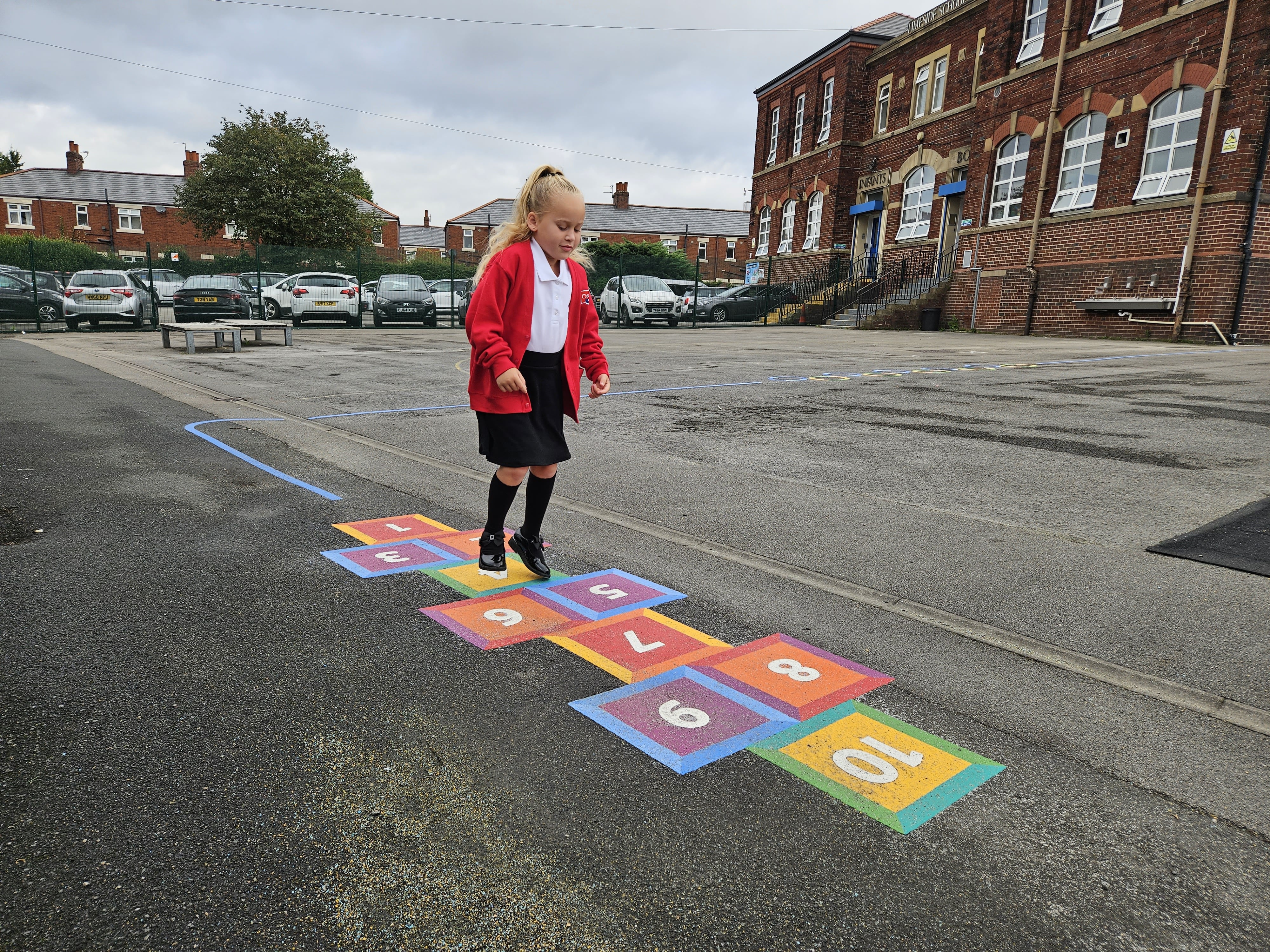 A little girl is hopping along a hopscotch that has been installed on a tarmac playground.