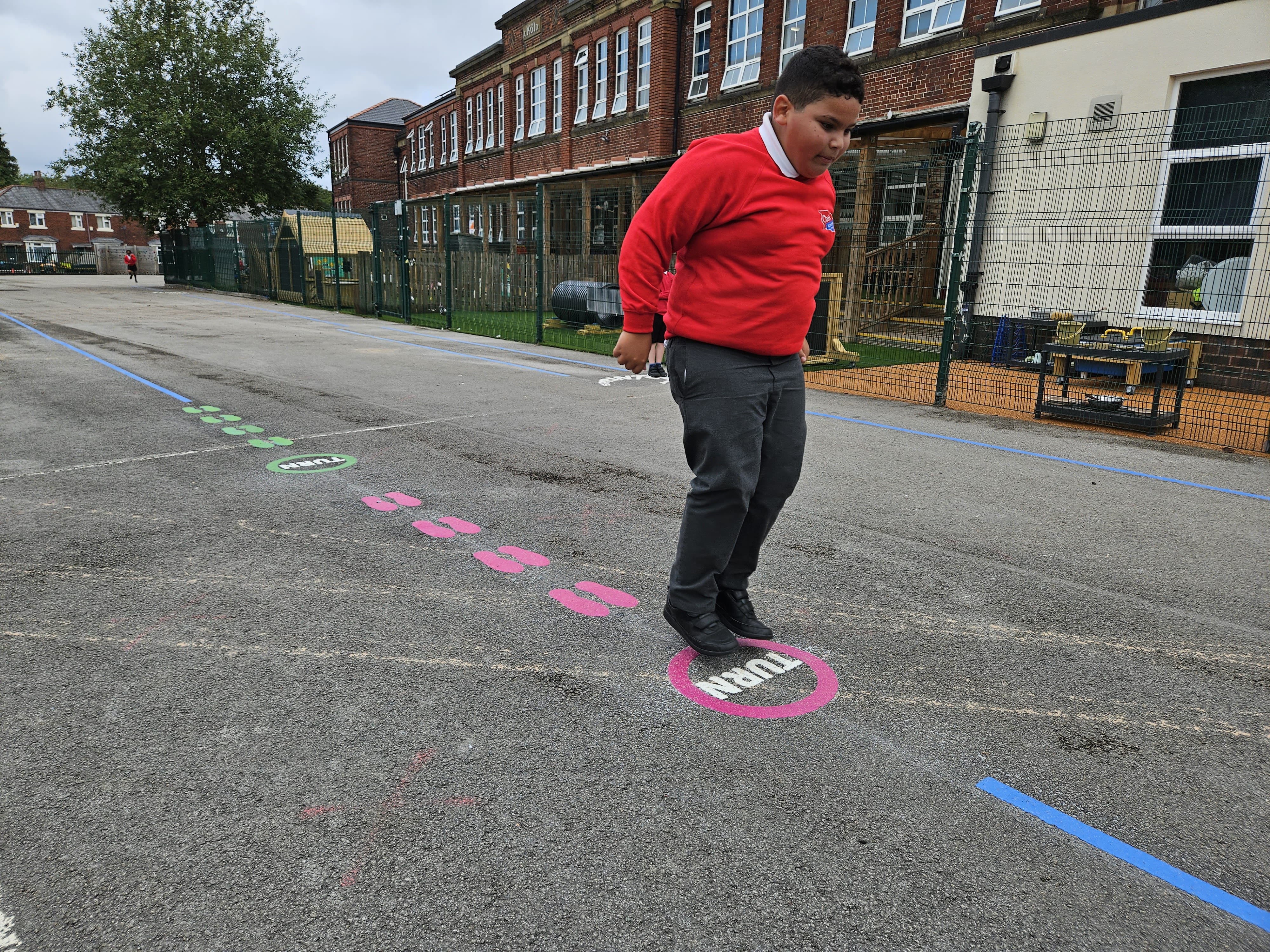 A child is playing on a thermoplastic playground marking on a tarmac surface.