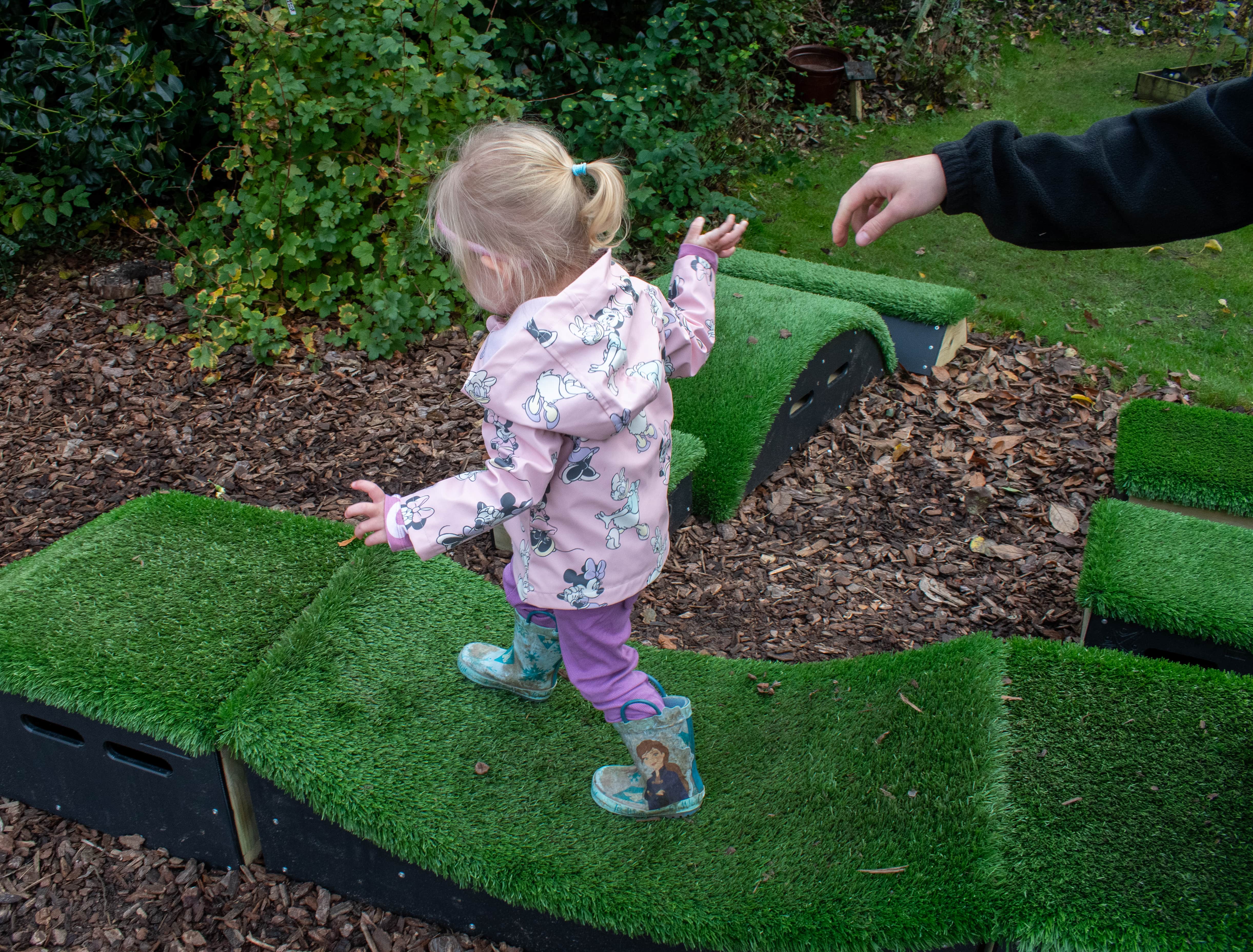 A little girl is traversing a set of Get Set, Go! Blocks as a teachers hand can be seen leaving her side.