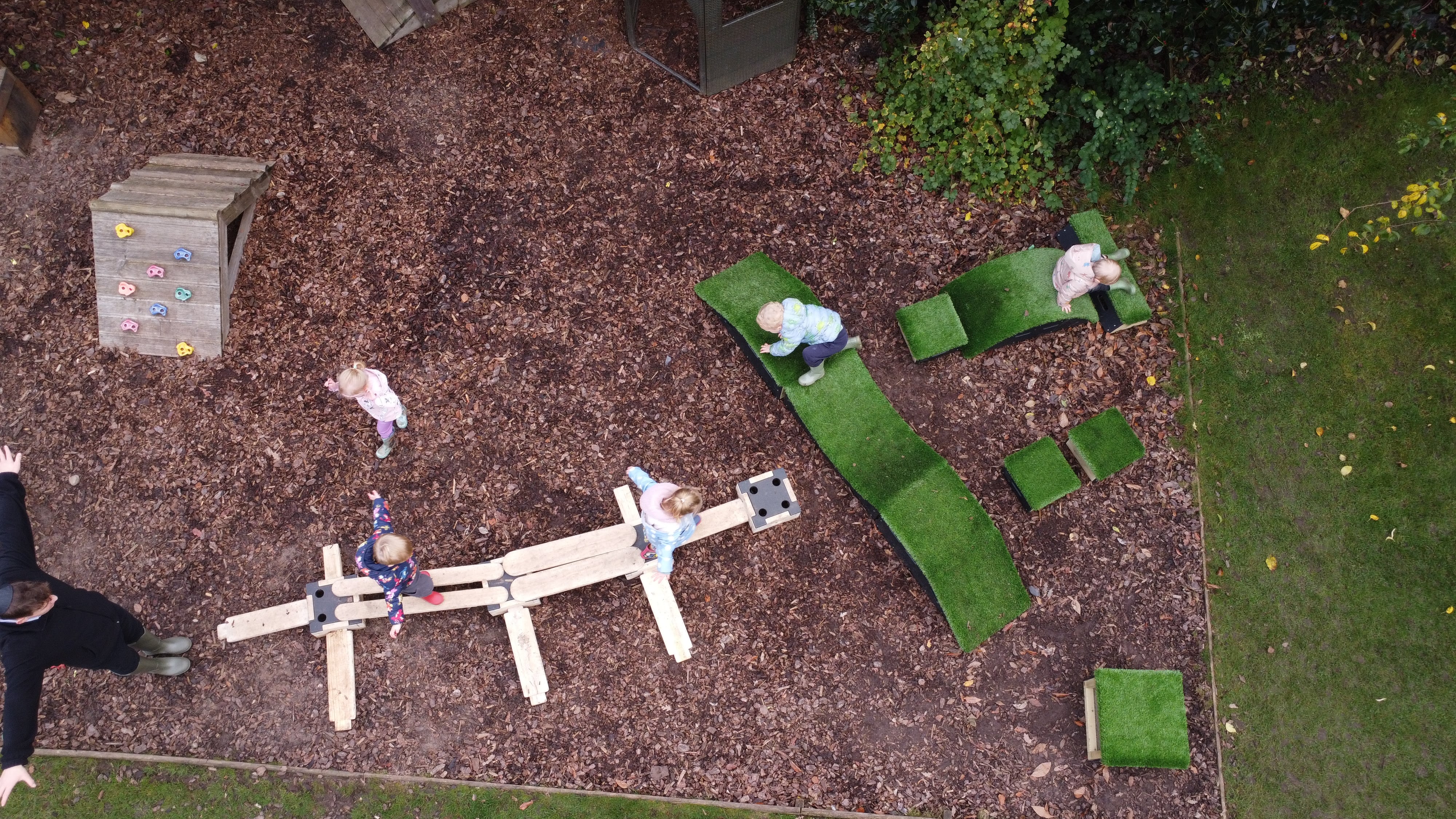 A group of children are exploring the Play Builder set and Get Set, Go! Blocks. A nursery practitioner is stood at the front of the Play Builder and is guiding the children across.