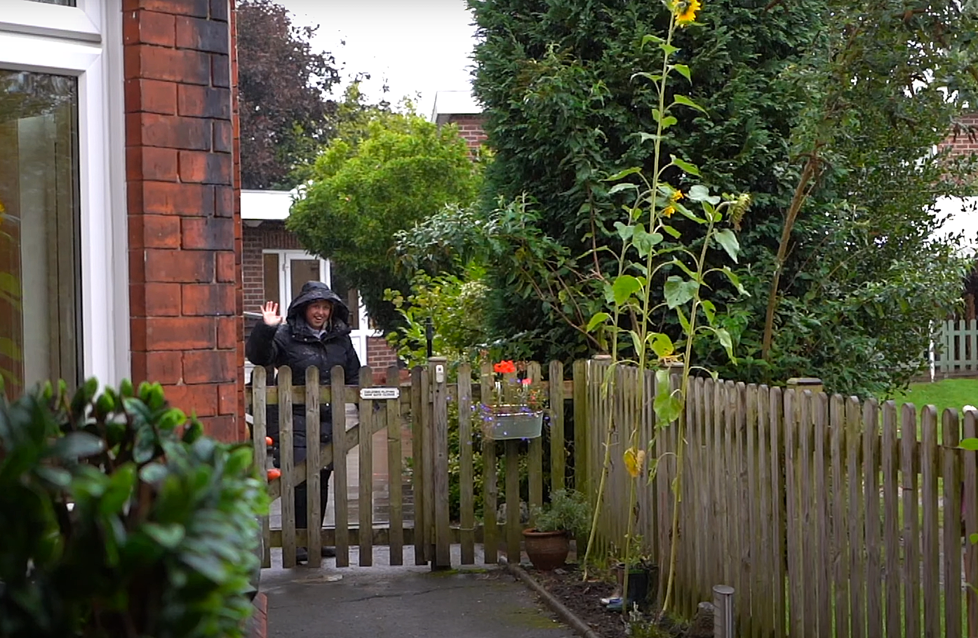 A staff member from Rosebank Nursery is stood at a wooden gate and is waving at the camera