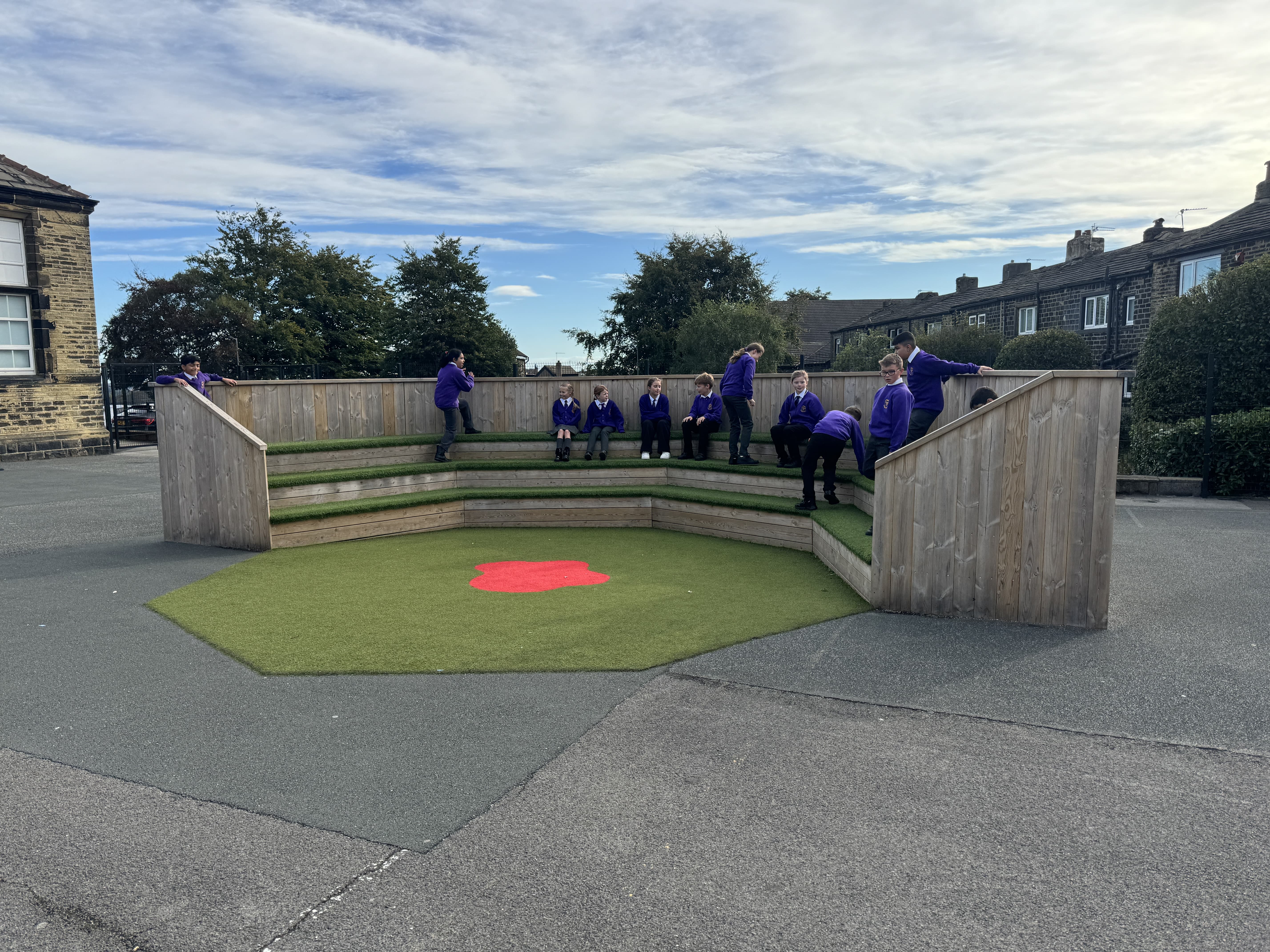 A performance area that has been created in the middle of a tarmac playground. The design is an amphitheatre, with a safety surface coloured green and red in the centre. 