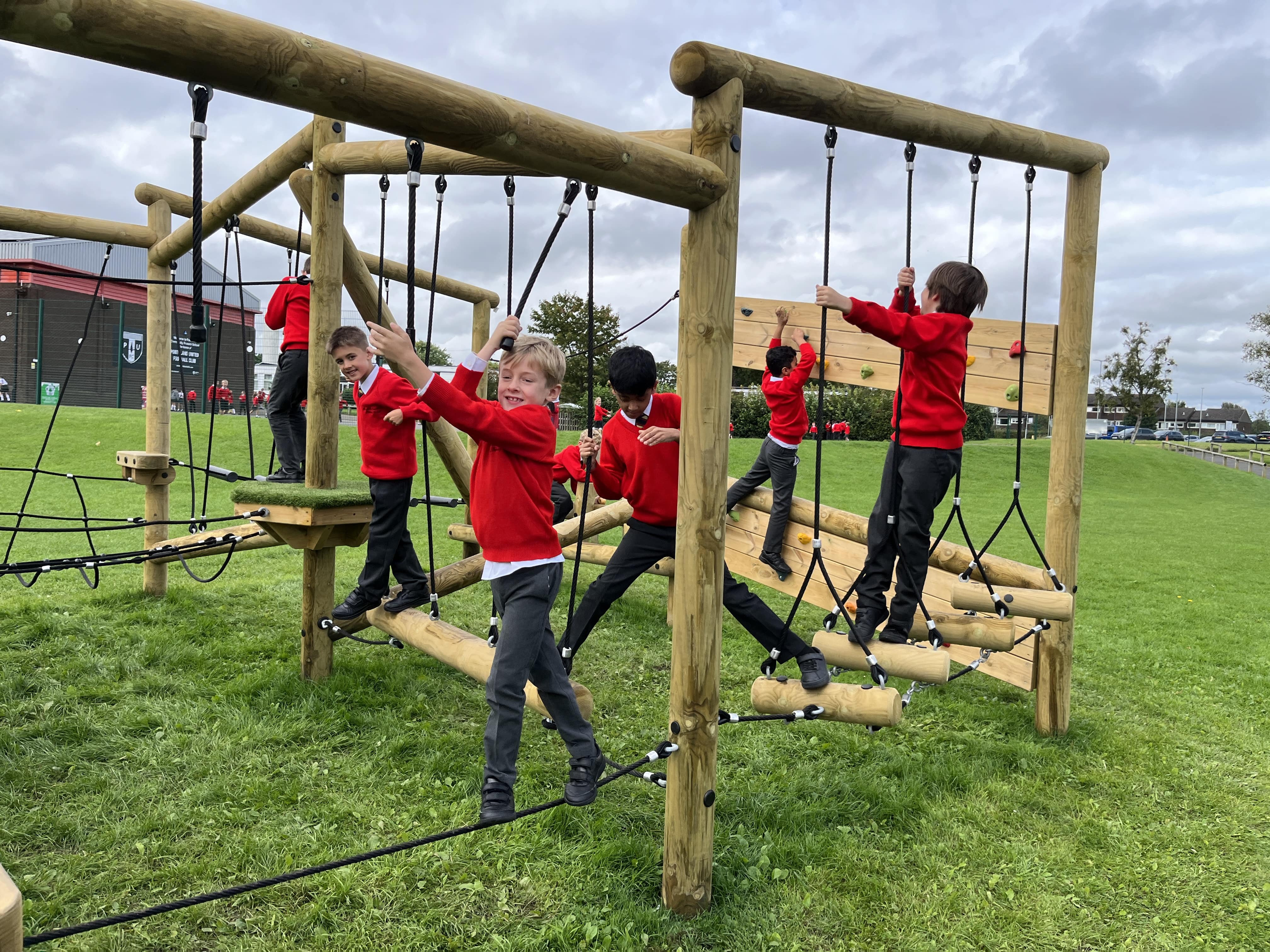 A group of children are playing on a trim trail and tackling a variety of different challenges. The children look ecstatic and are fully immersed in the equipment.