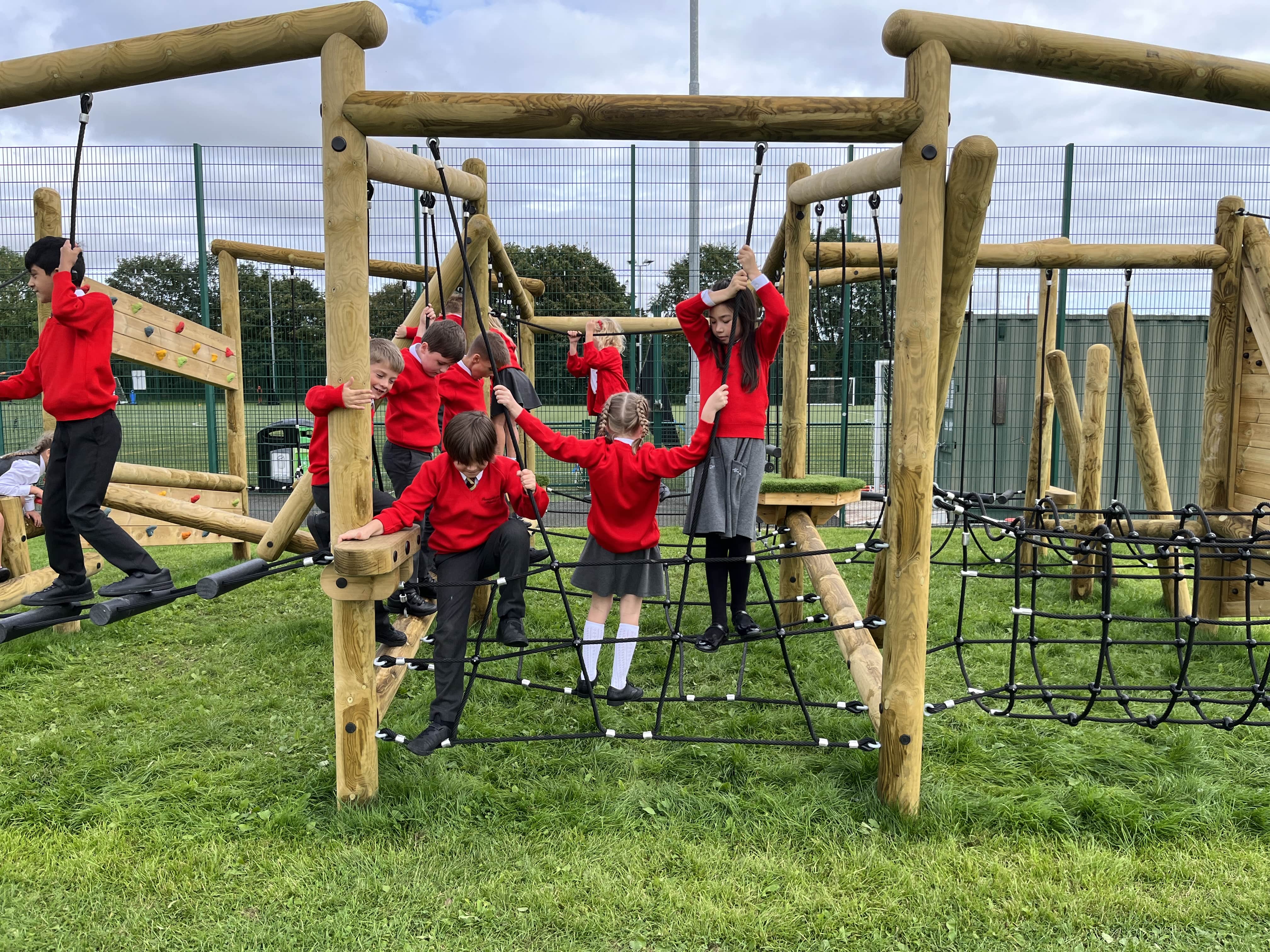 A group of children are exploring the rope bridge on the Grizedale Forest Circuit and are making their way across the equipment. Other children can be seen in the background, tackling different challenges.