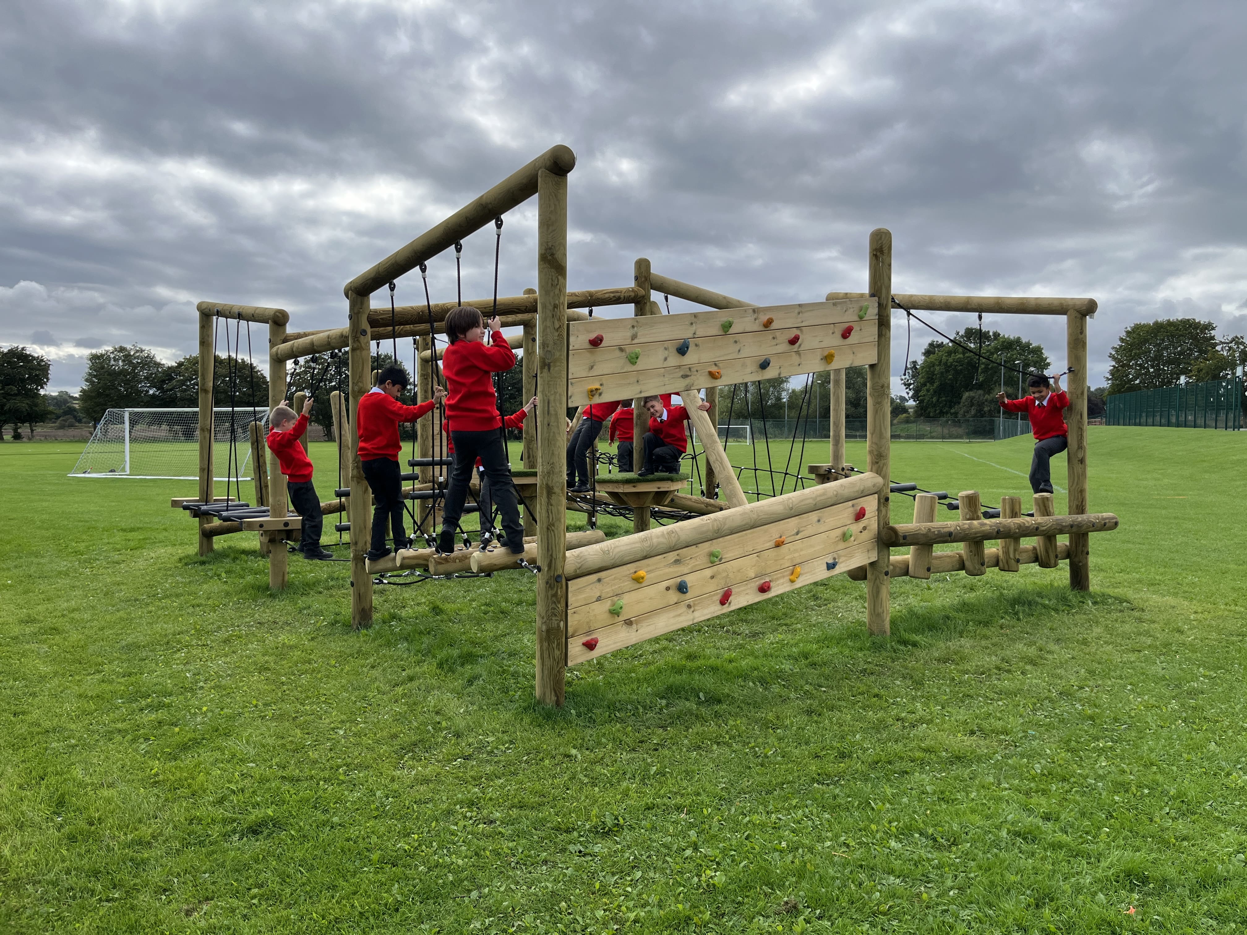 A large group of children are climbing around the Grizedale Forest Circuit, tackling unique challenges and working together to accomplish it.