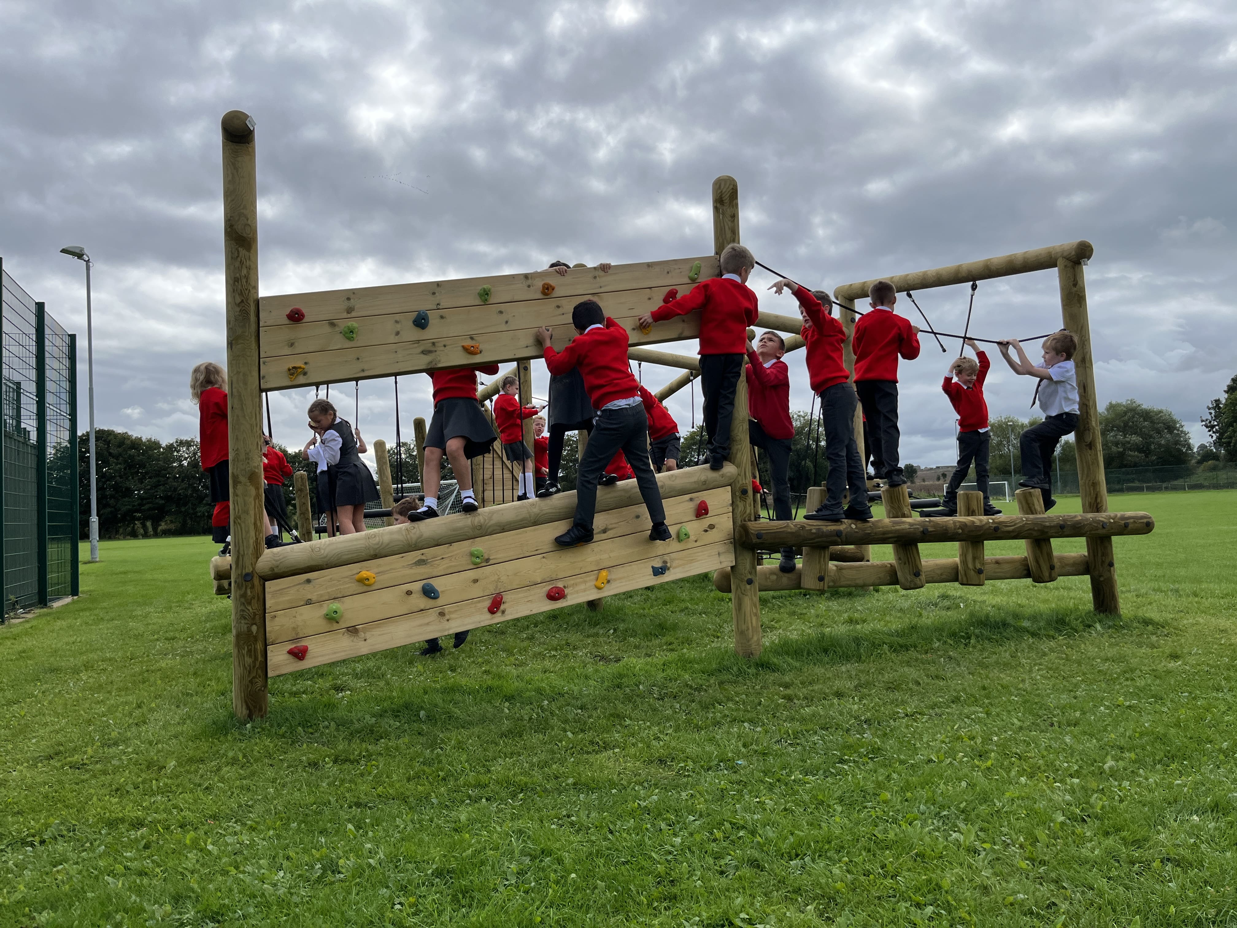 A group of children are completing an active play Forest Circuit and are approaching the climbing wall. The children are in a single file line as they wait their turn.