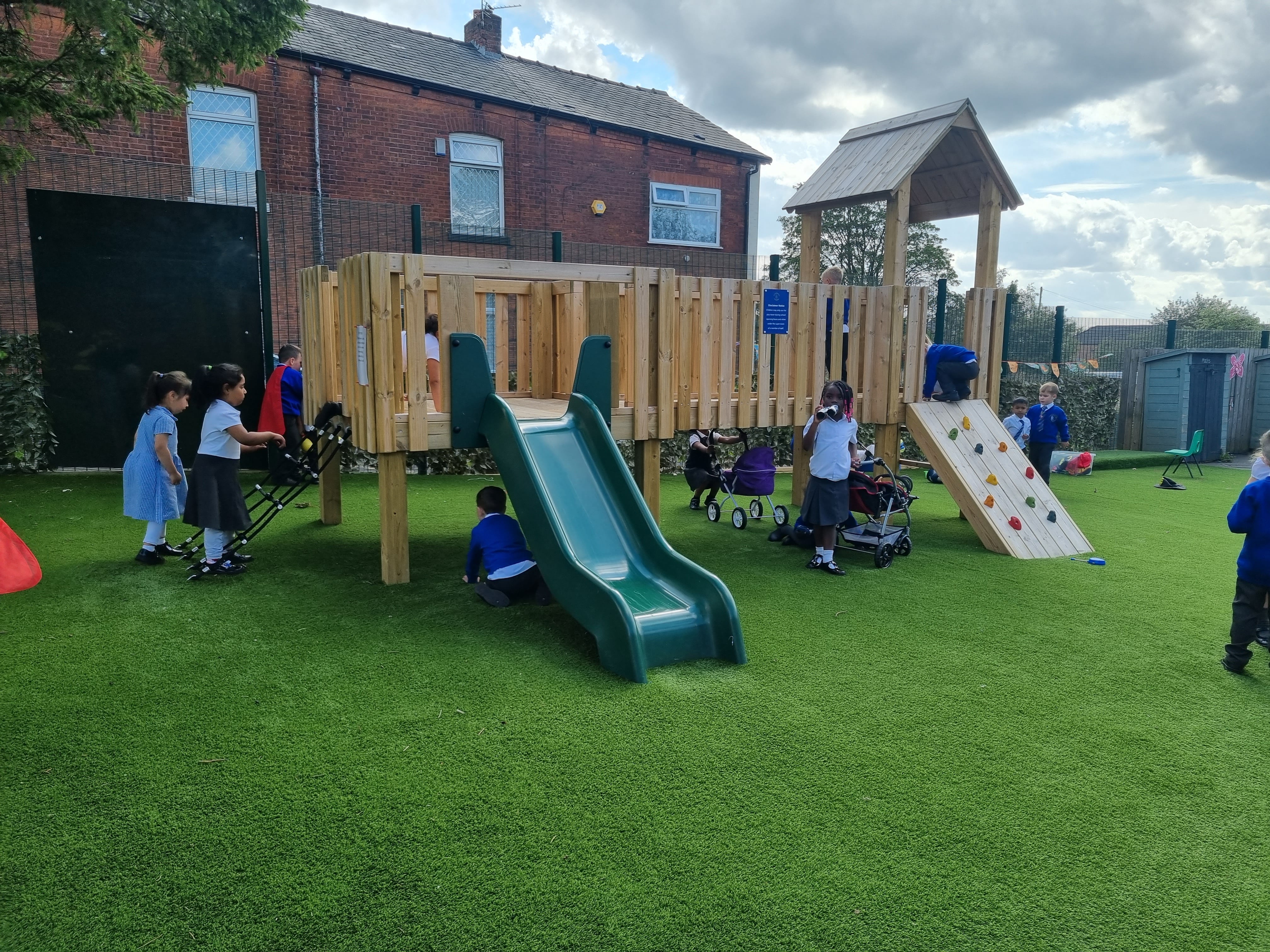 A modular play tower has been installed on top of an artificial grass playturf surface. The surface is a deep green colour.