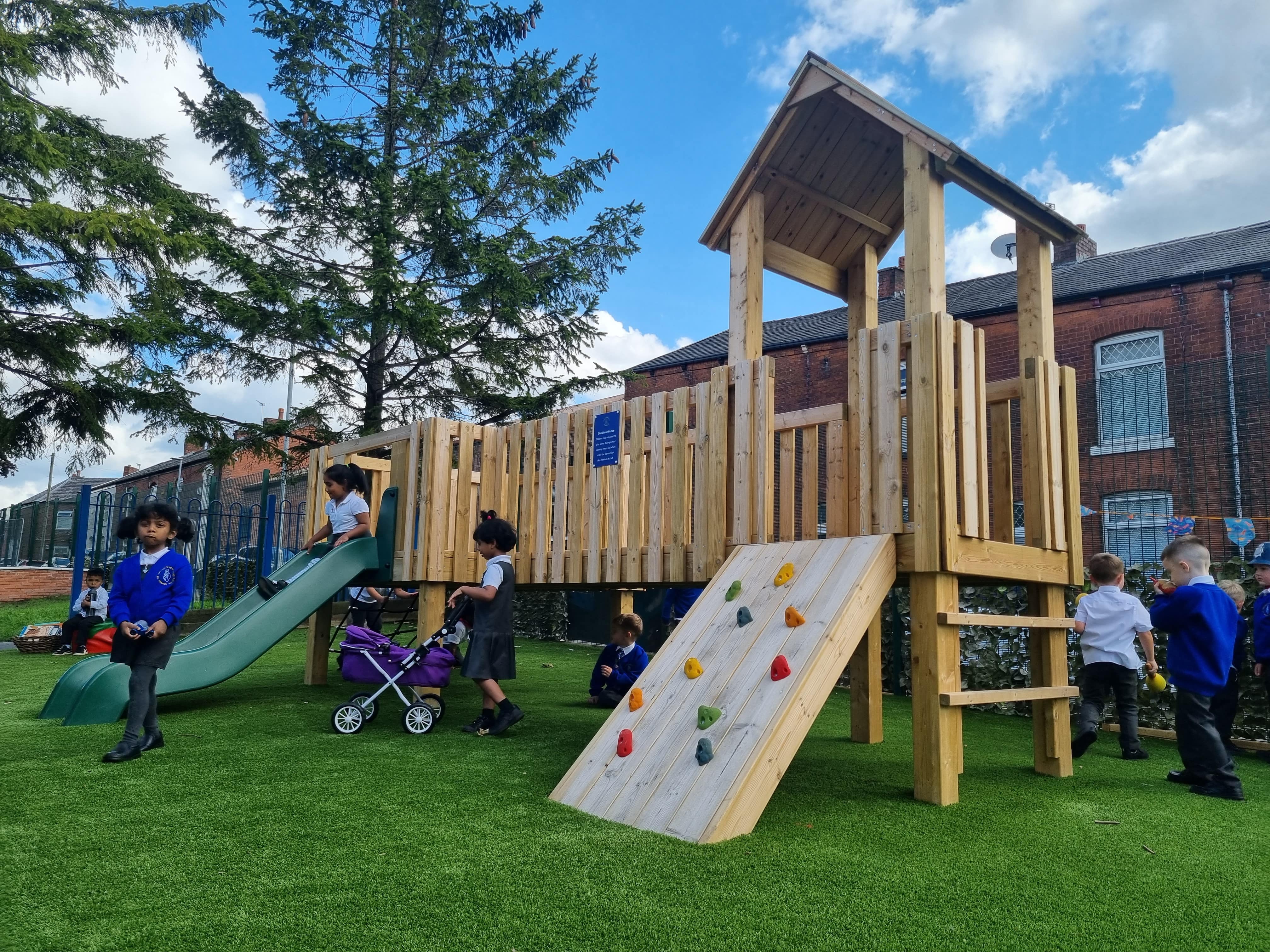 The Kenilworth Modular Play Tower standing tall on an artificial grass surface. A group of children are playing all around the equipment.