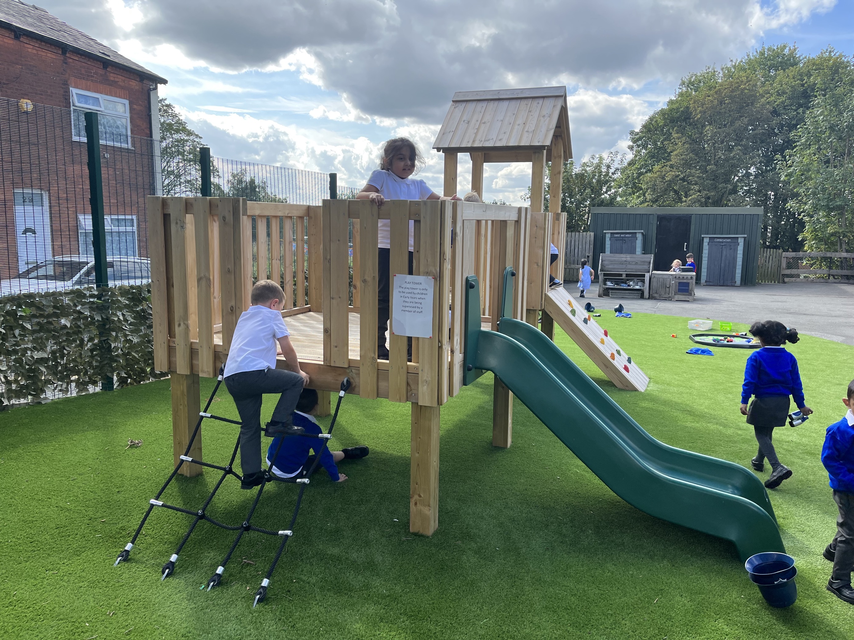 A group of children are climbing up the Kenilworth Modular Play Tower and playing with each other.