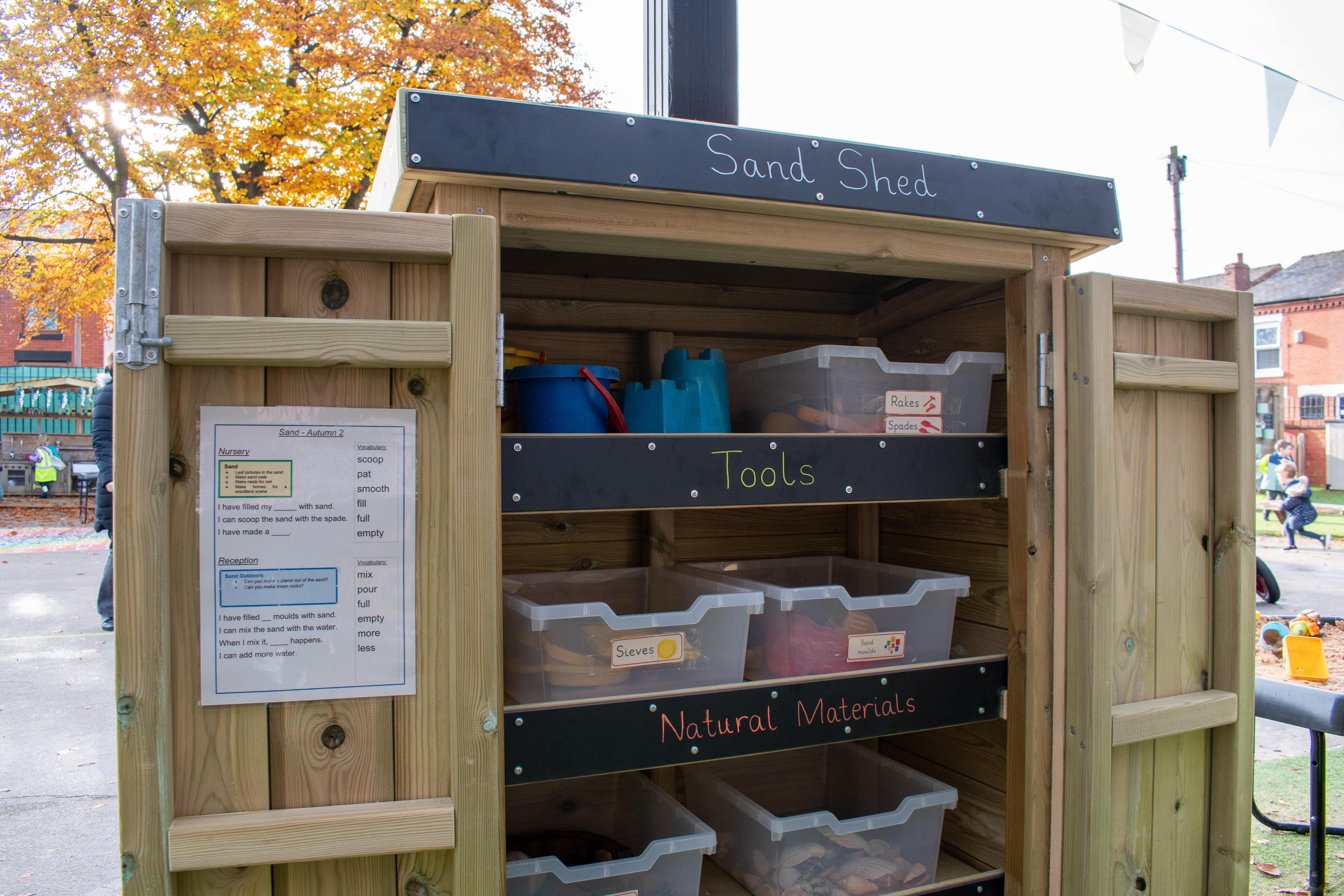 An open Acorn Self-Select Store with the title of "Sand Shed". Within the shed, a variety of plastic tubs can be seen containing different sand play resources.