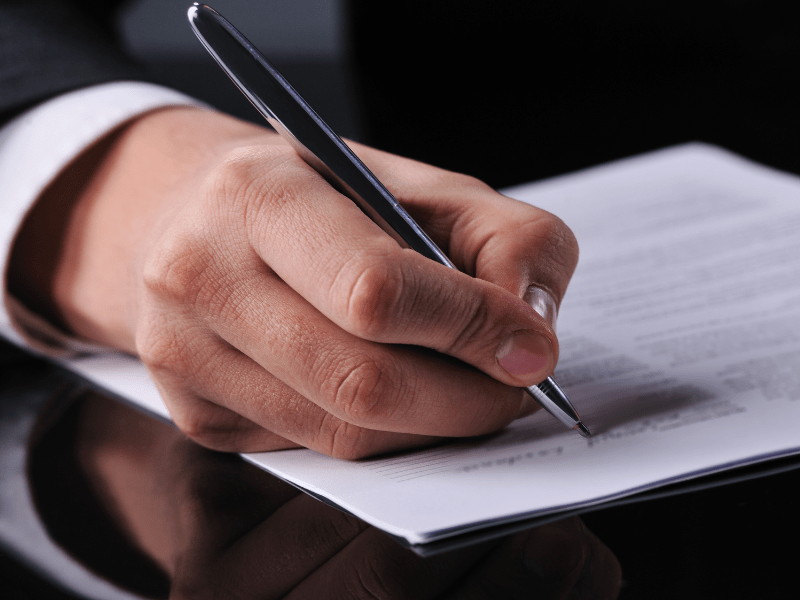 A man's hand signing a document with a black pen.