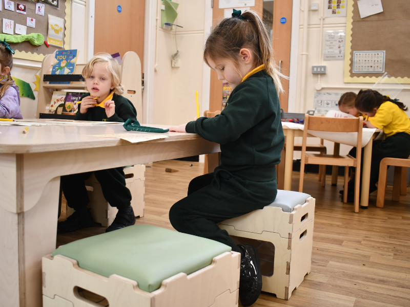 A little girl is completing her work whilst sat at a table within an EYFS classroom.