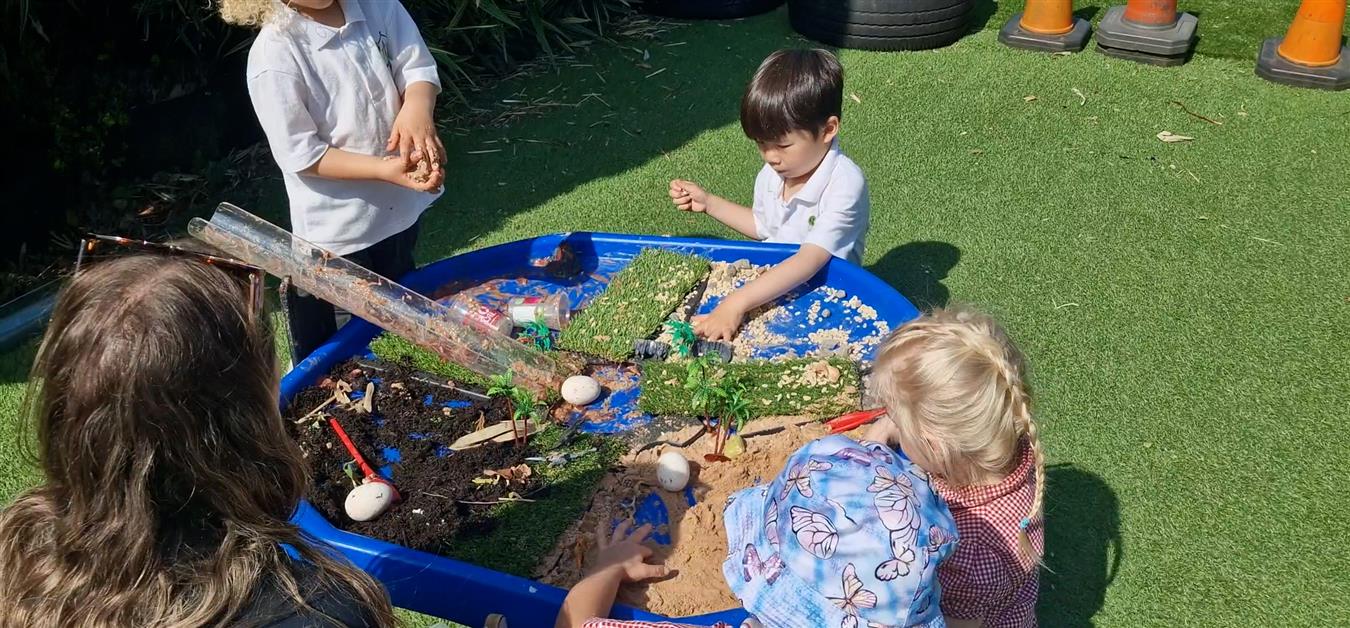 Four children are playing with a tuff table and are engaging in sensory play. The children look fully engaged with the activity.