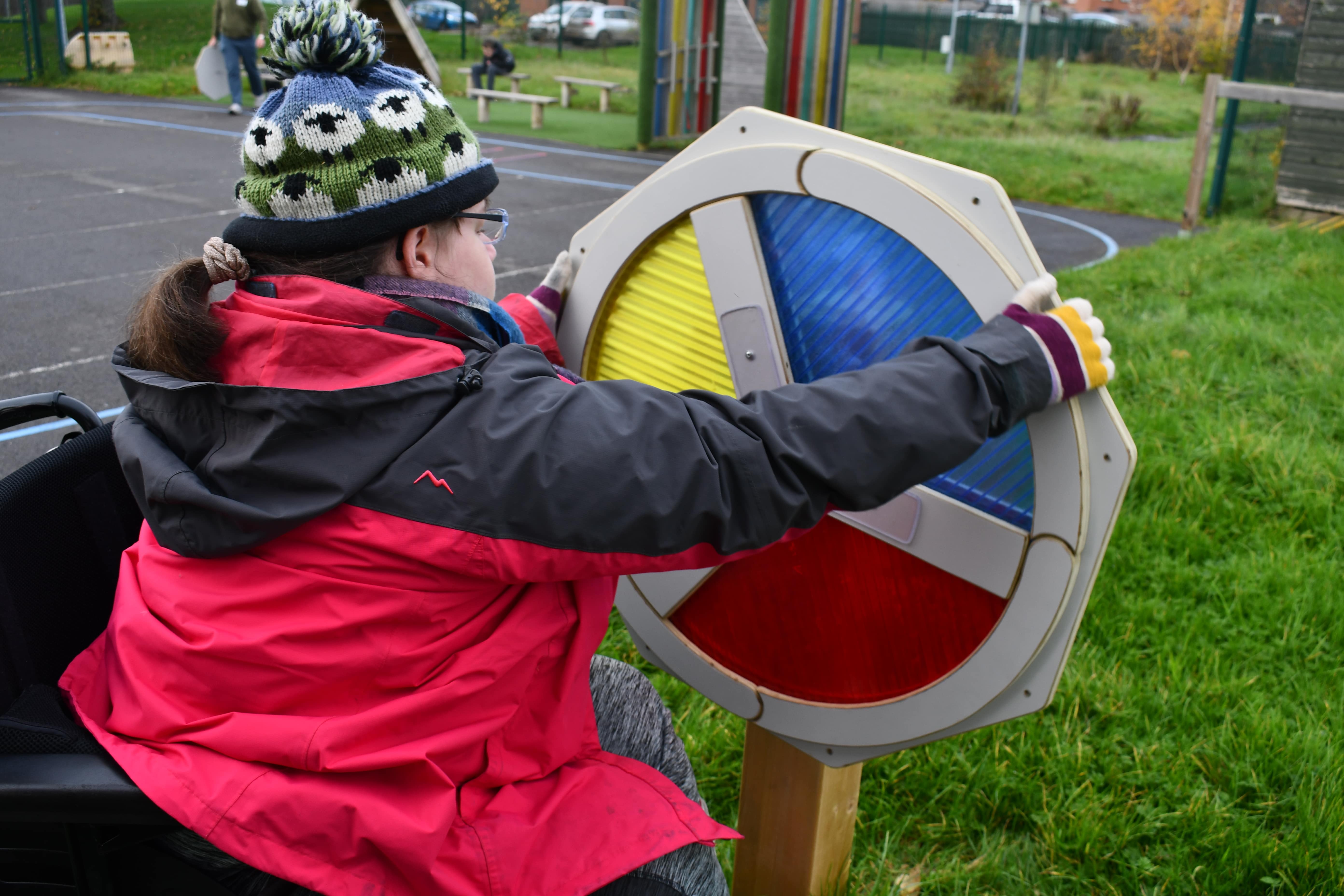 A little girl is holding a sensory spinner and is giving it a spin. You can see yellow, blue and red thirds on the spinner, all being made out of different materials.