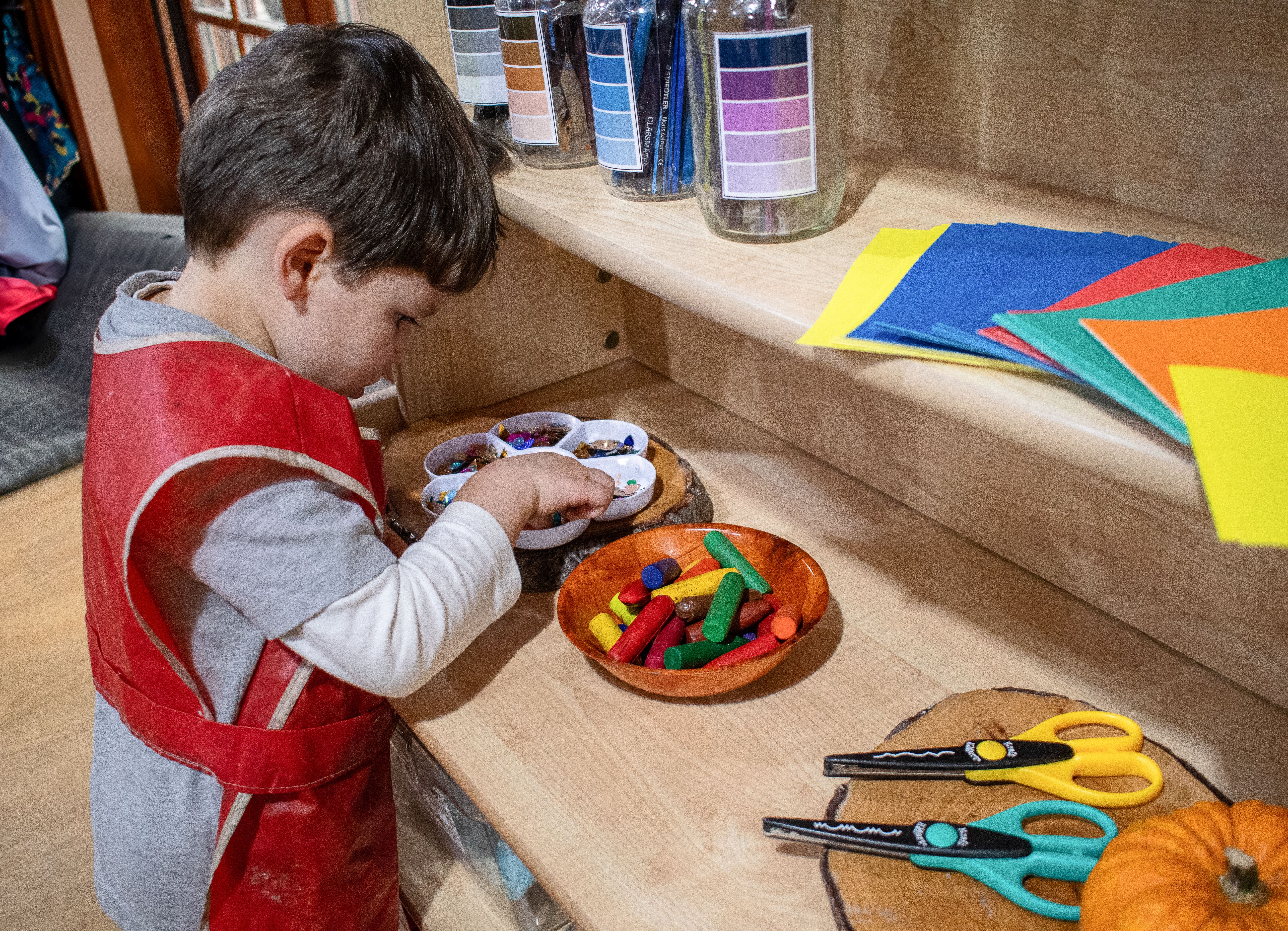 A boy is retrieving some arts and crafts materials from a Millhouse Welsh Dresser. The boy looks fascinated with the materials.