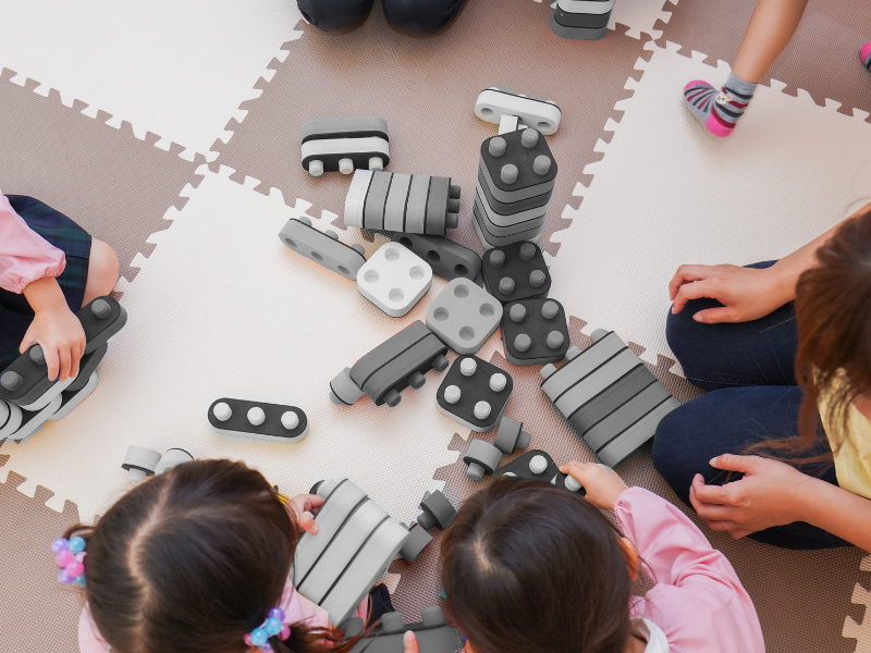 A group of children are sat on the floor and are playing with building blocks that are black and white.