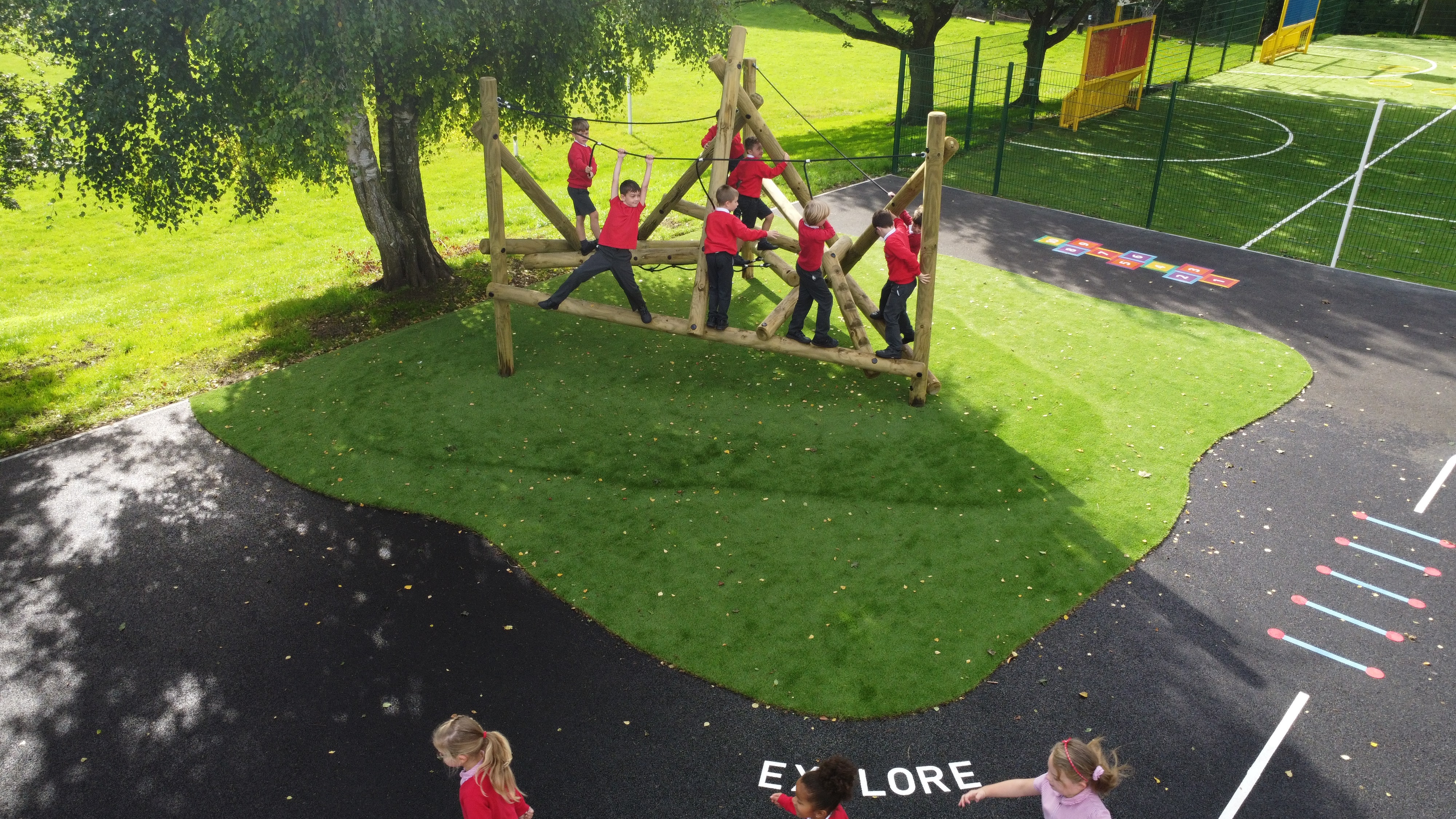 A small group of children are on top of the Bowfell Climber, which has been installed on artificial grass on the tarmac playground.