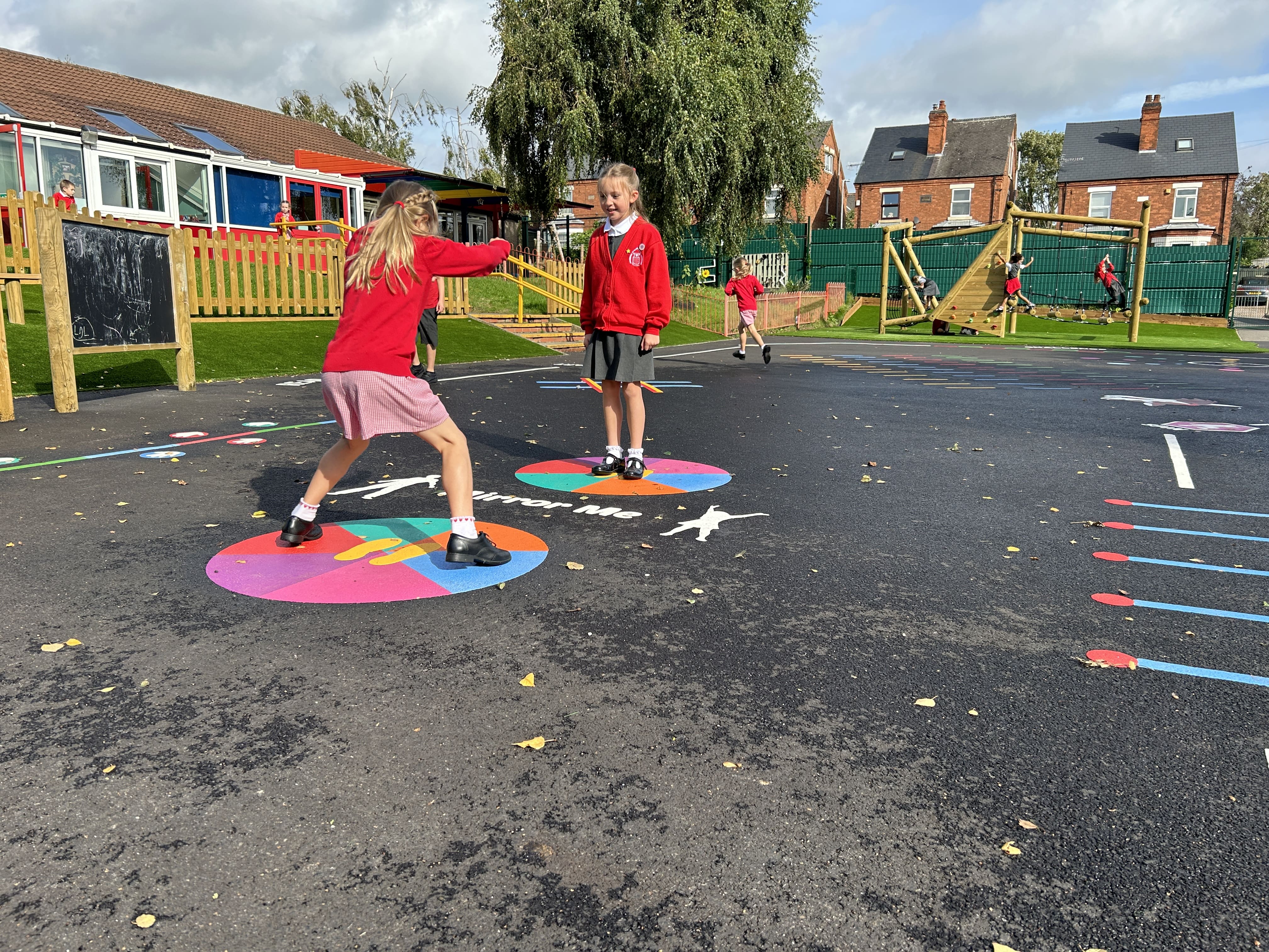 Two girls are playing on two thermoplastic playground markings whilst smiling and laughing.