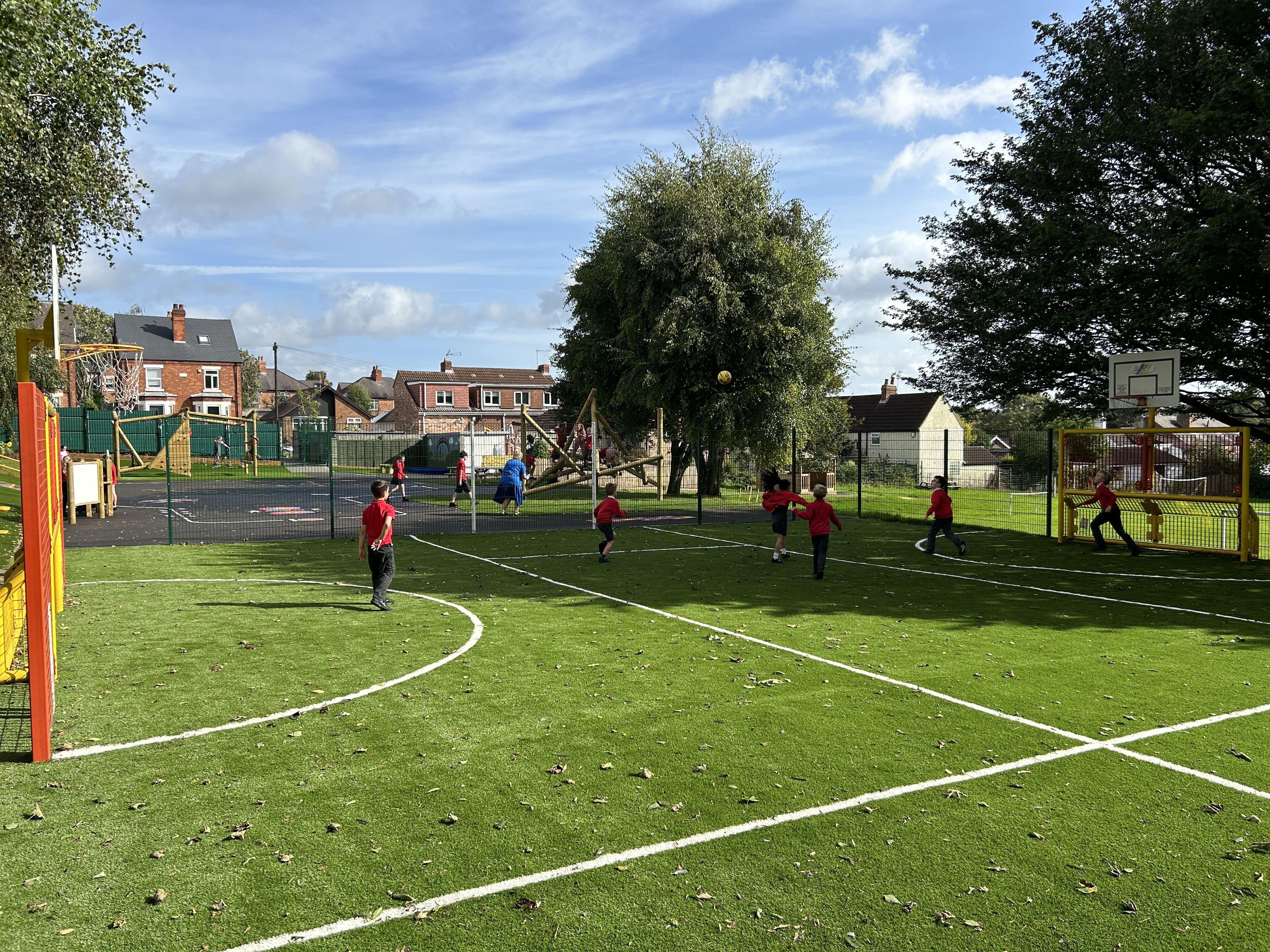 An artificial MUGA pitch with children playing a game of football on it.