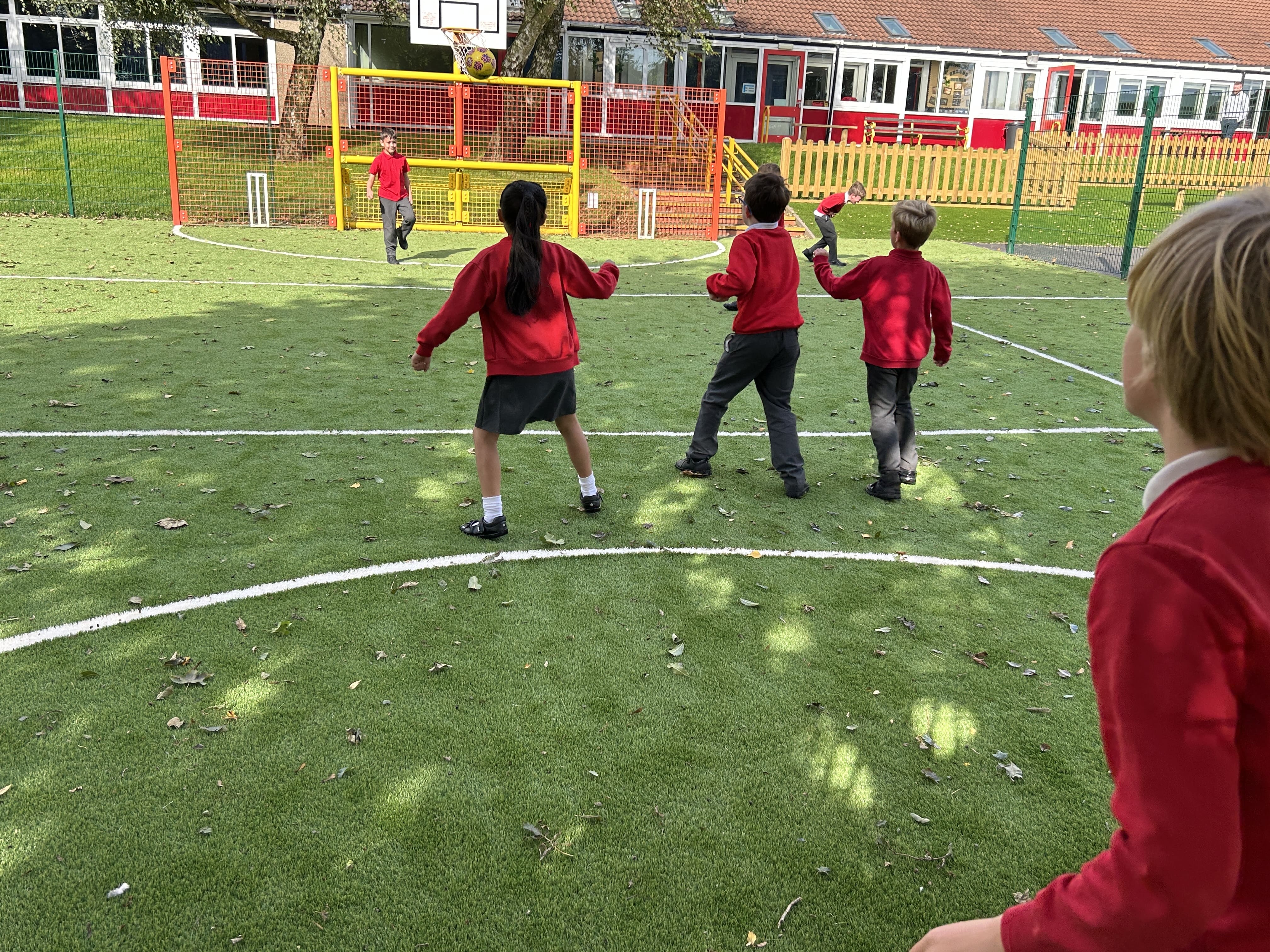 A group of children are celebrating a goal on a MUGA pitch, surrounded by colourful steel fencing.