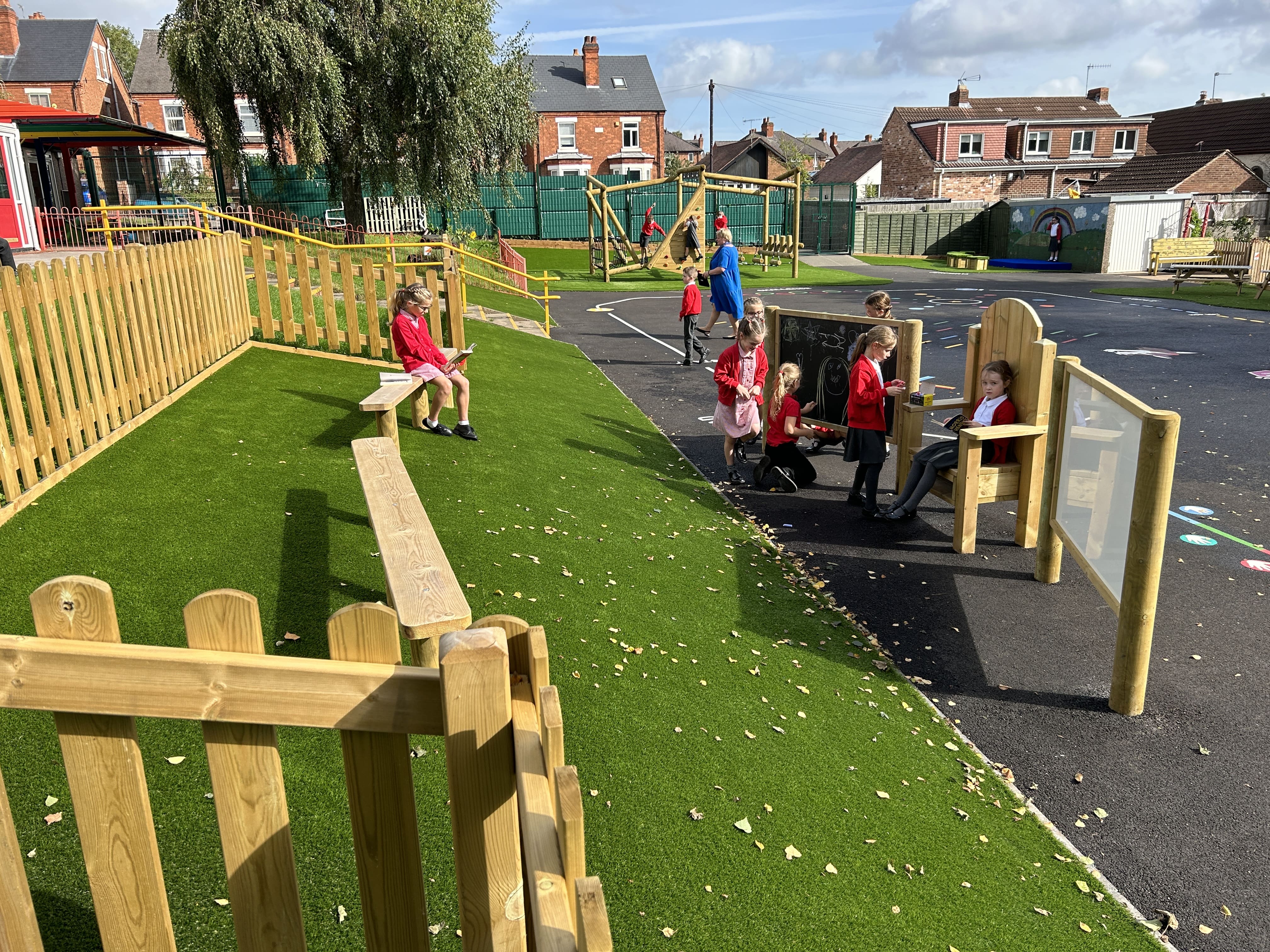 An artificial grass surface with some benches installed on it, which are facing a freestanding chair and a whiteboard and chalkboard.