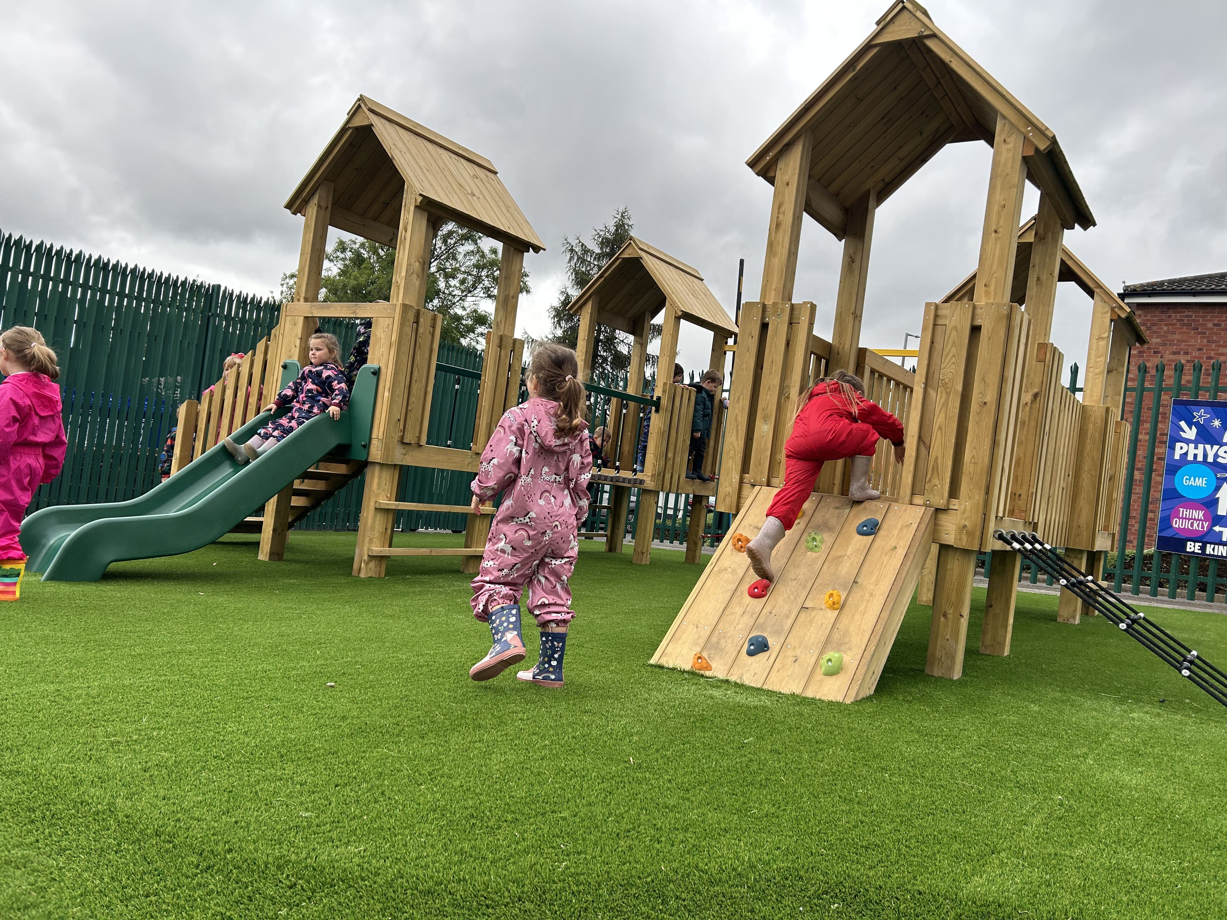 A little boy is climbing up a ramp whilst a little girl is walking on the artificial grass.