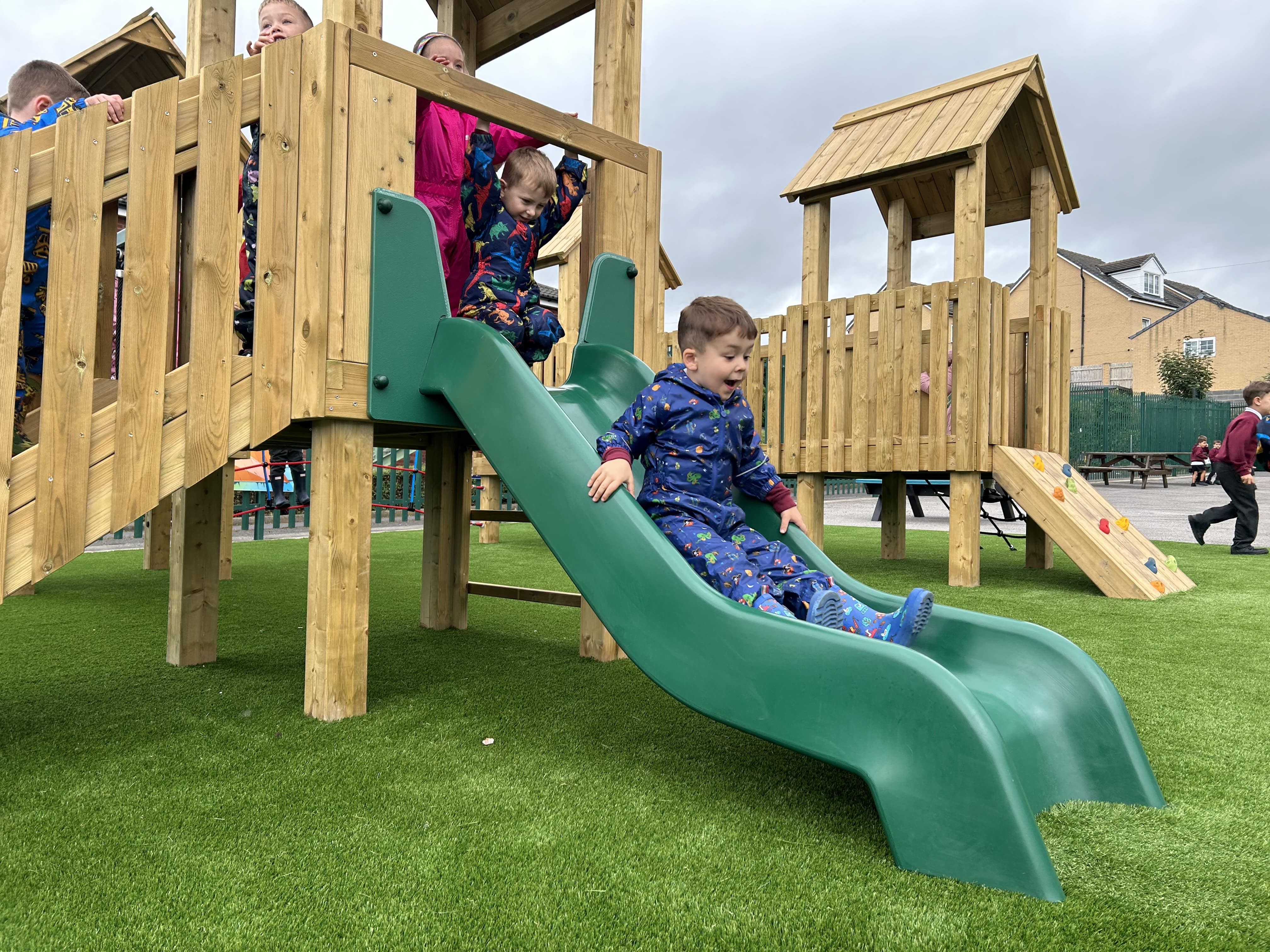 A little boy is sliding down a green slide that is connected to a play tower