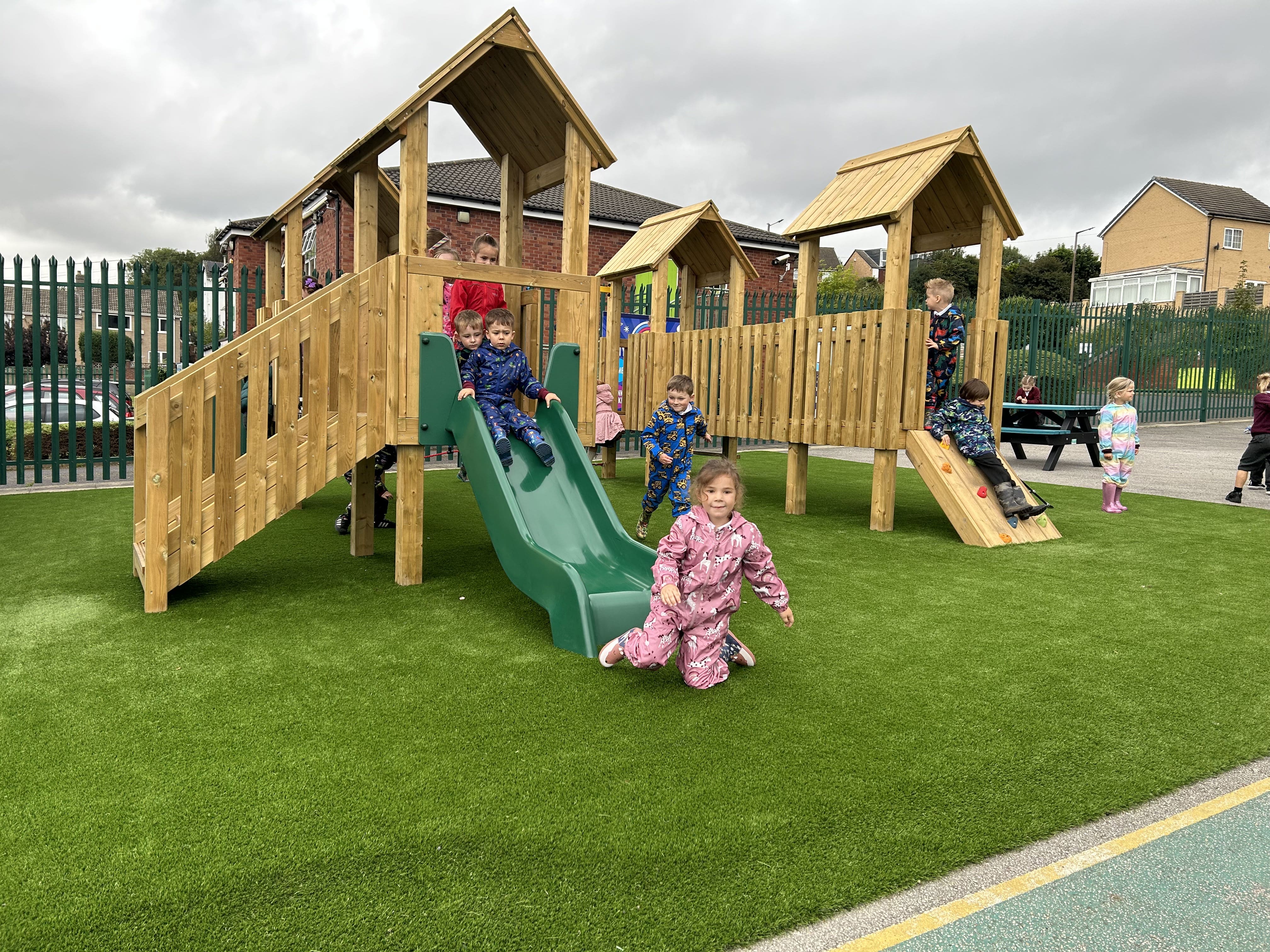 A group of children are going down a green slide that is connected to a Play Tower.