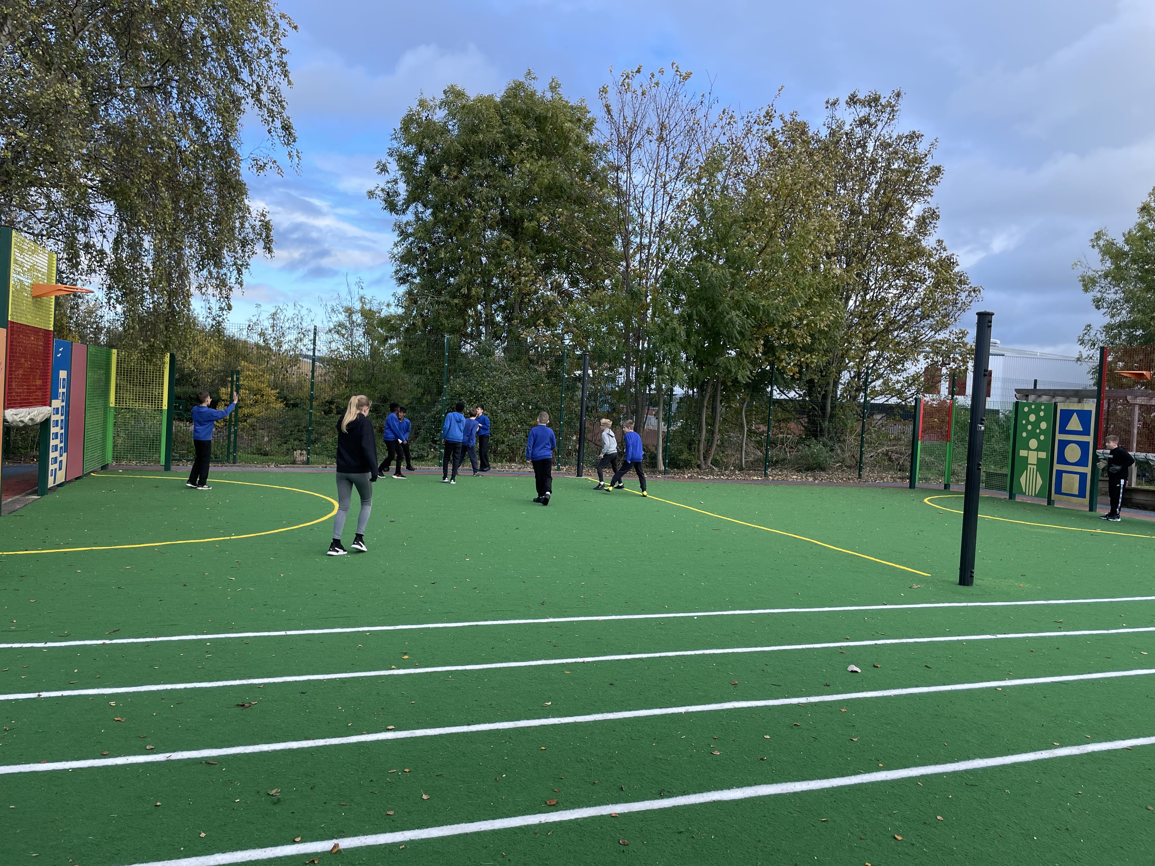 A group of children are playing a game of football on the green MUGA court