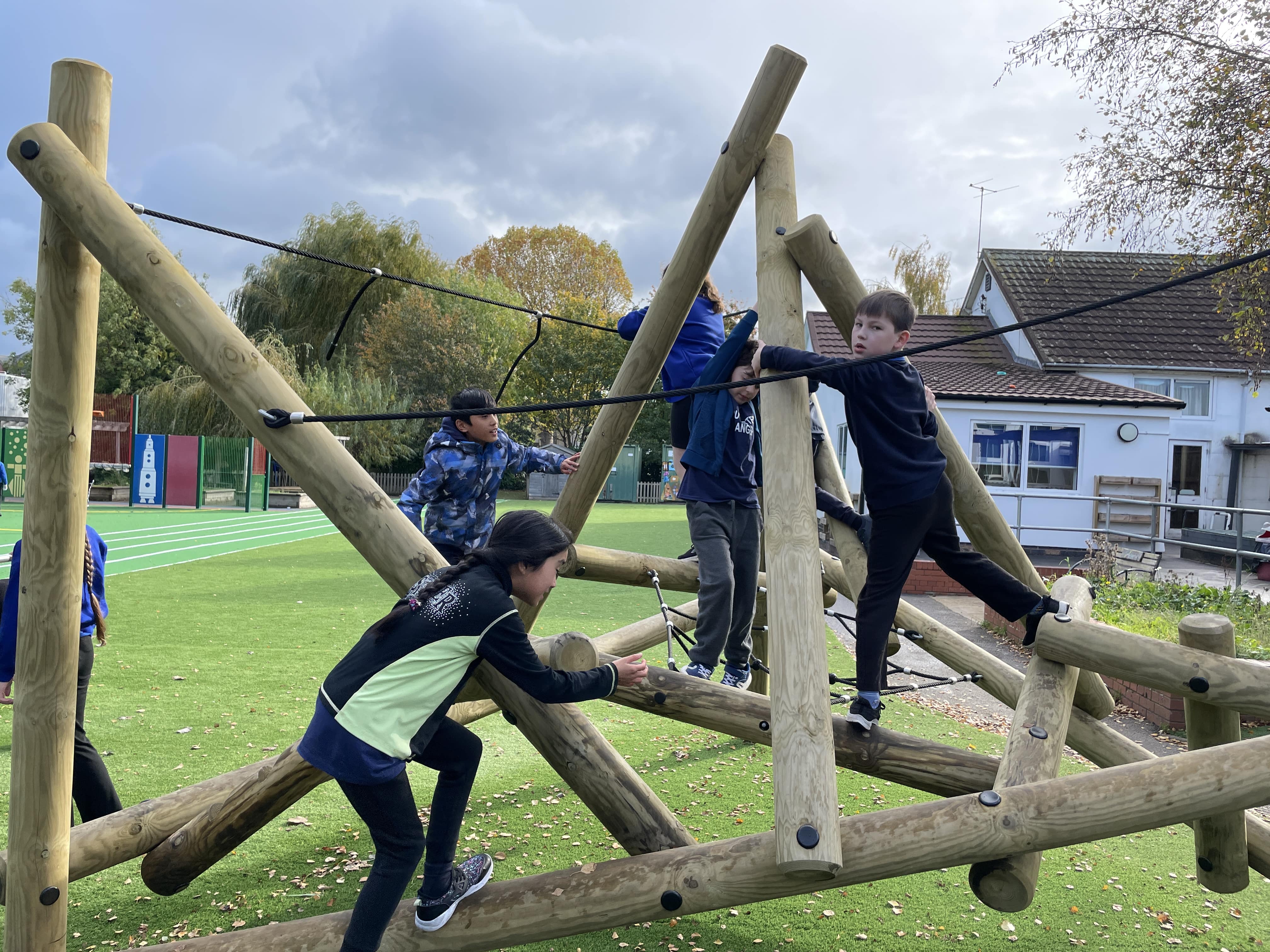 A small group of children are playing on a climbing frame, which has been installed on an artificial grass surface.