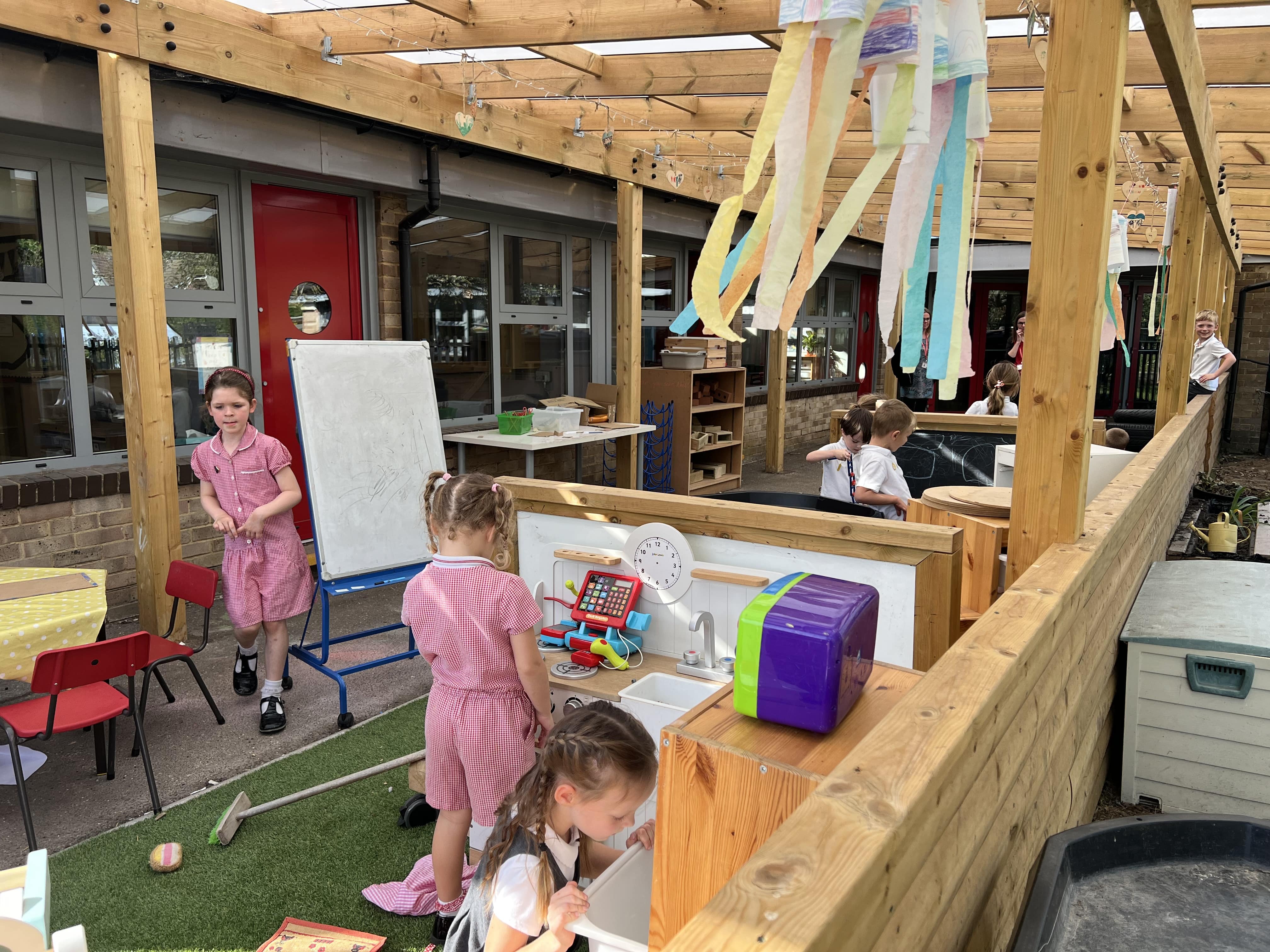 A small class of children are carrying out tasks in their outdoor classroom, filled with learning resources.