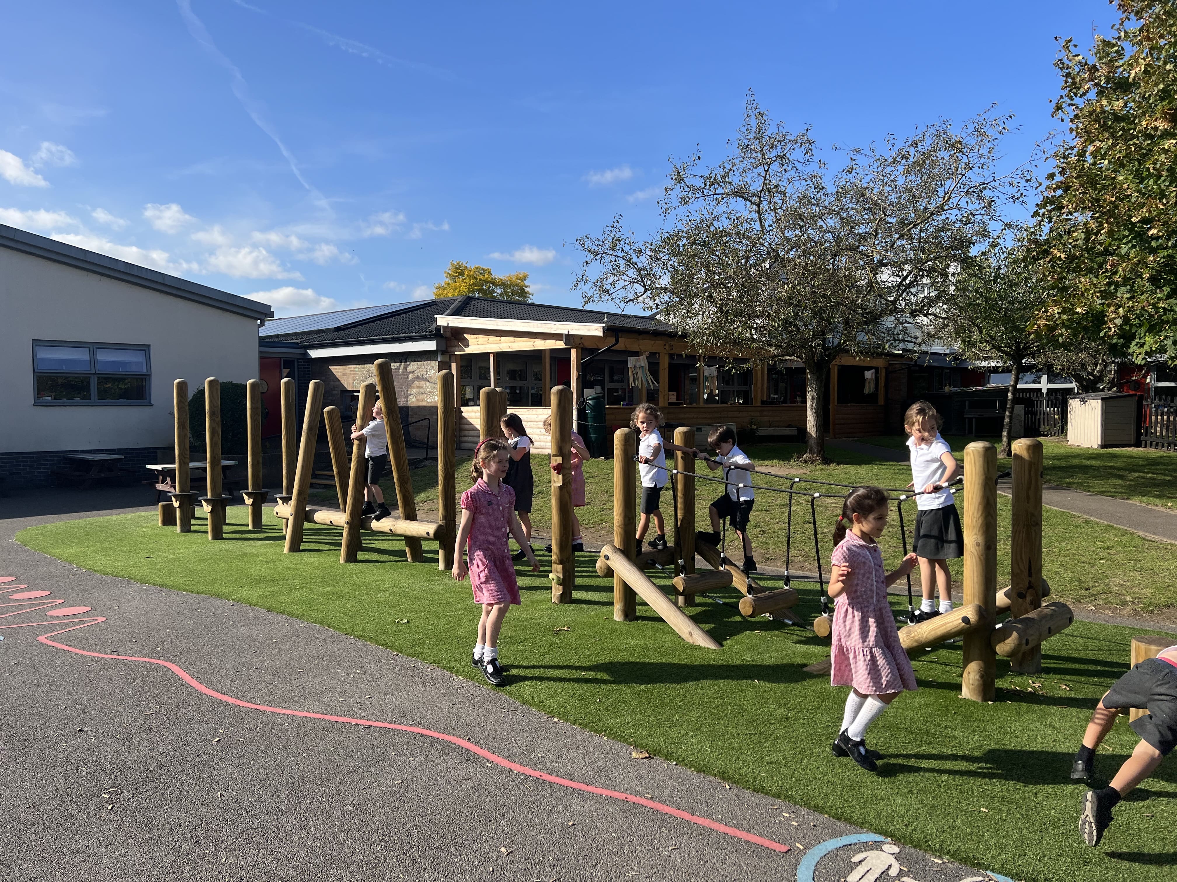 A large group of children are playing on a Trim Trail, which has been installed on artificial grass.