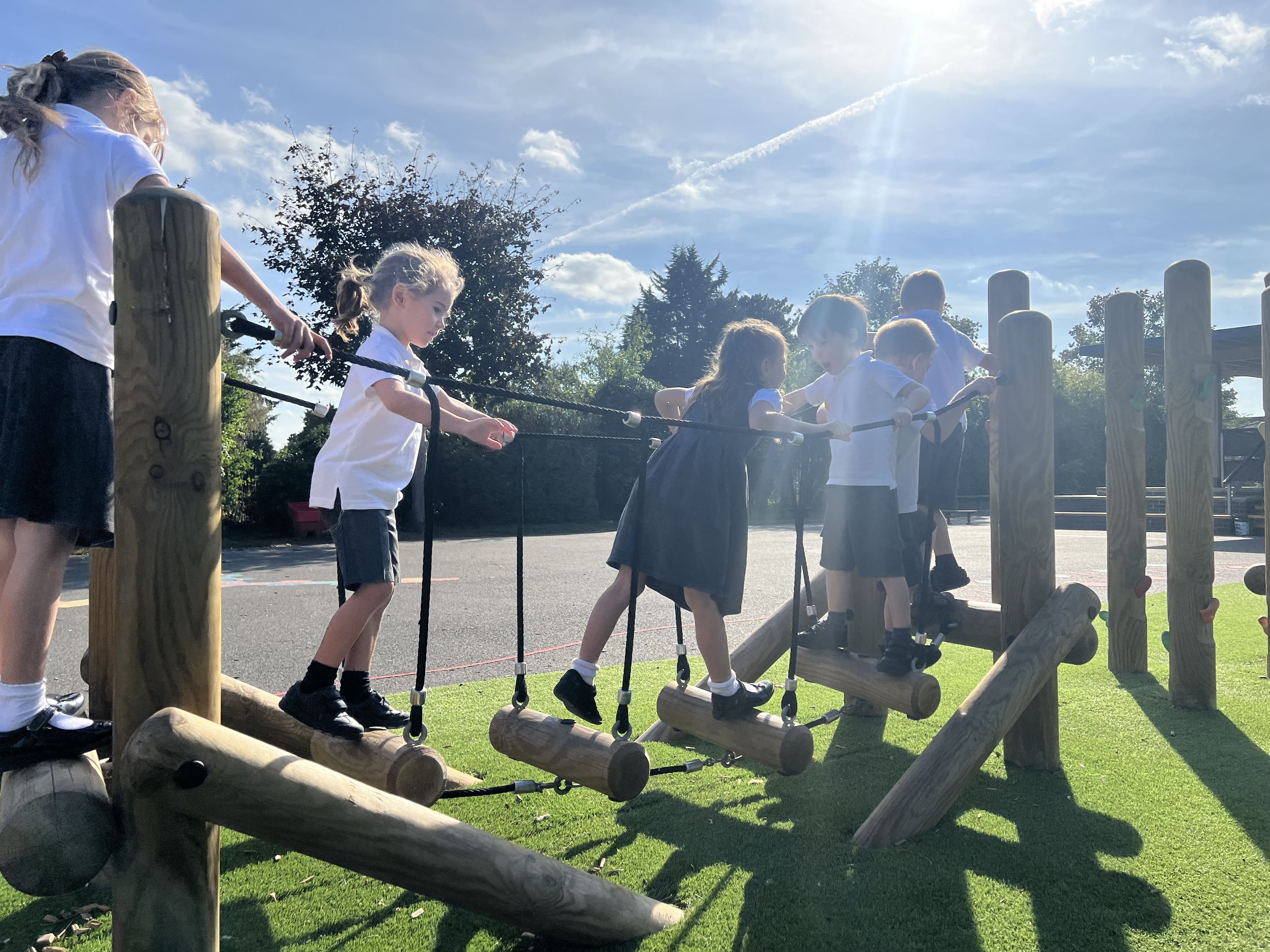 A group of children are navigating their way across a log bridge, which is a part of a Trim Trail.