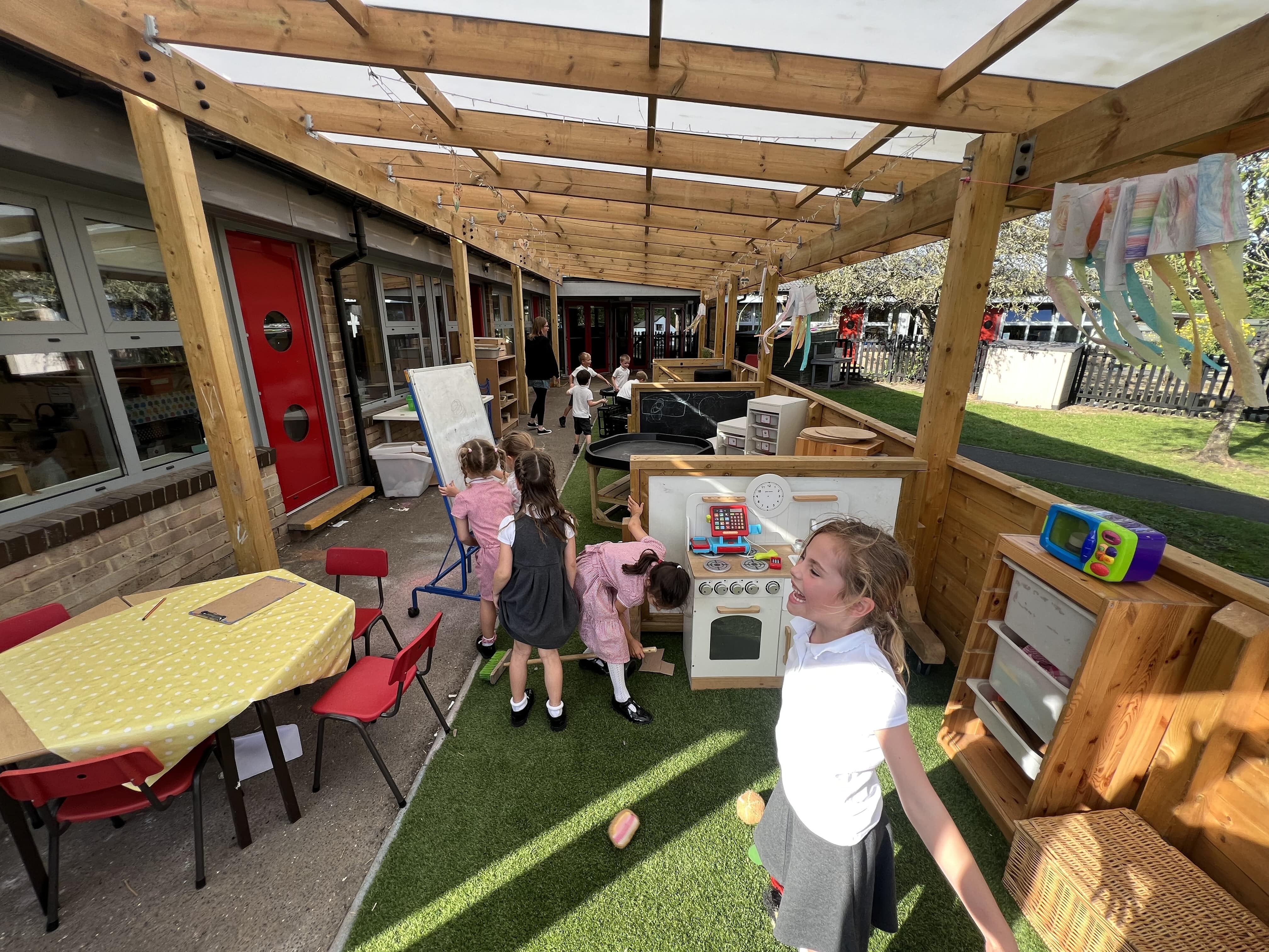 A group of children are underneath an outdoor canopy and are taking part in a creative lesson.