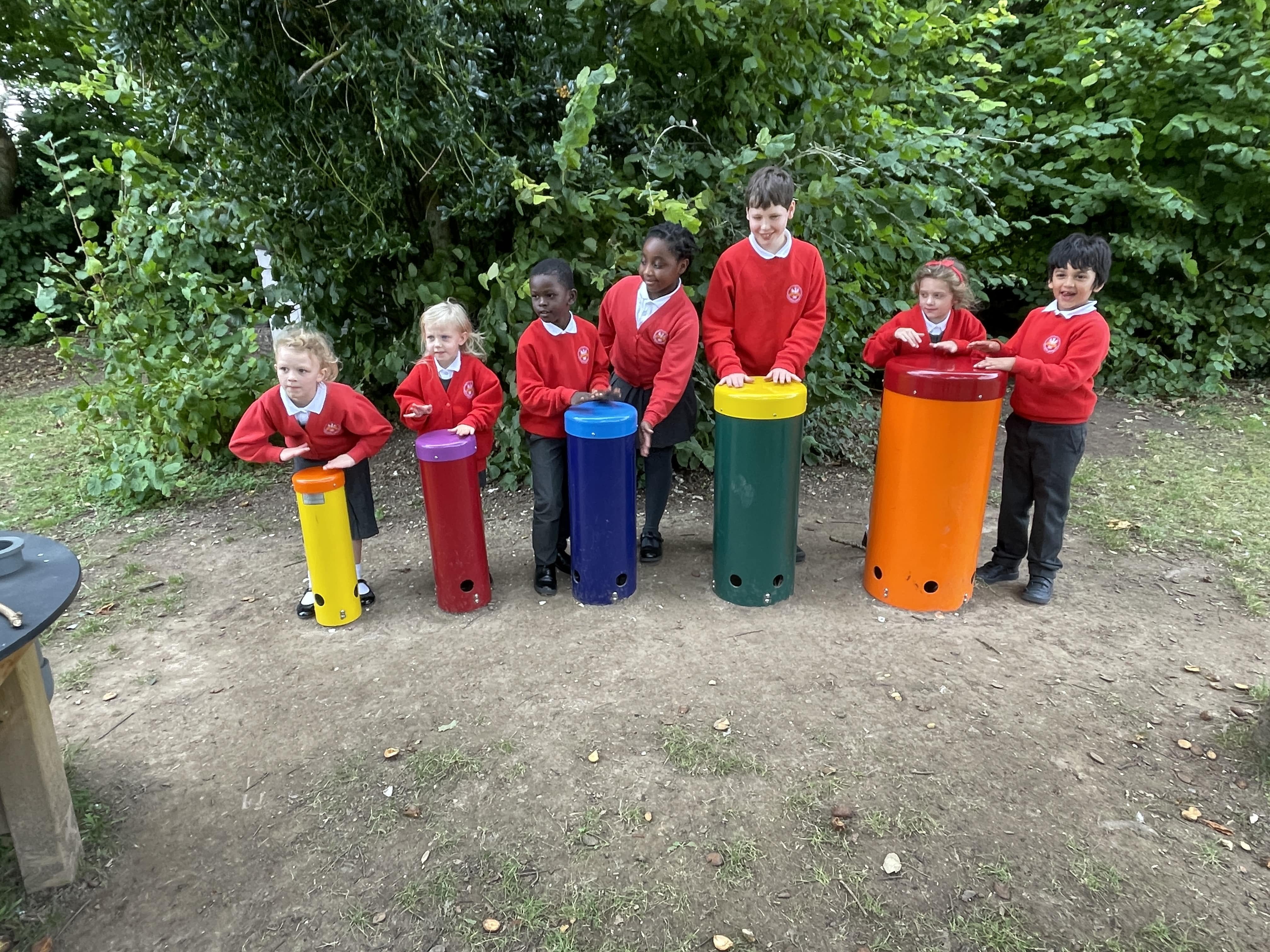 A group of children are playing with the African Drums and looking at the camera