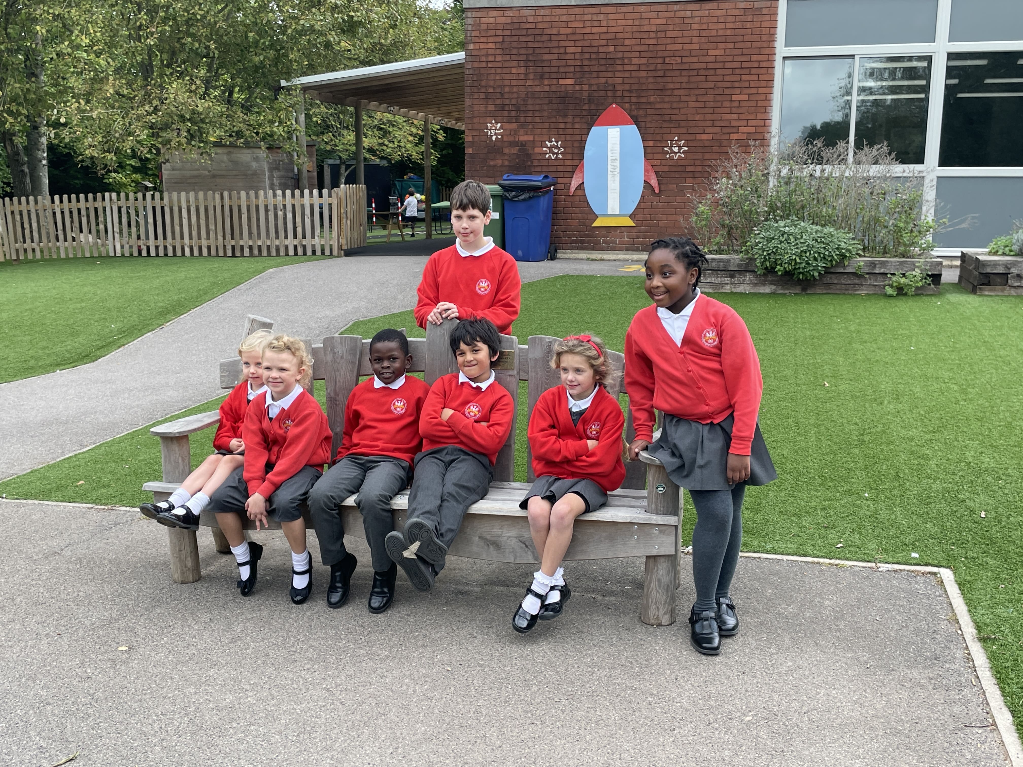 A group of children are sitting on a bench that has been placed on a tarmac playground.