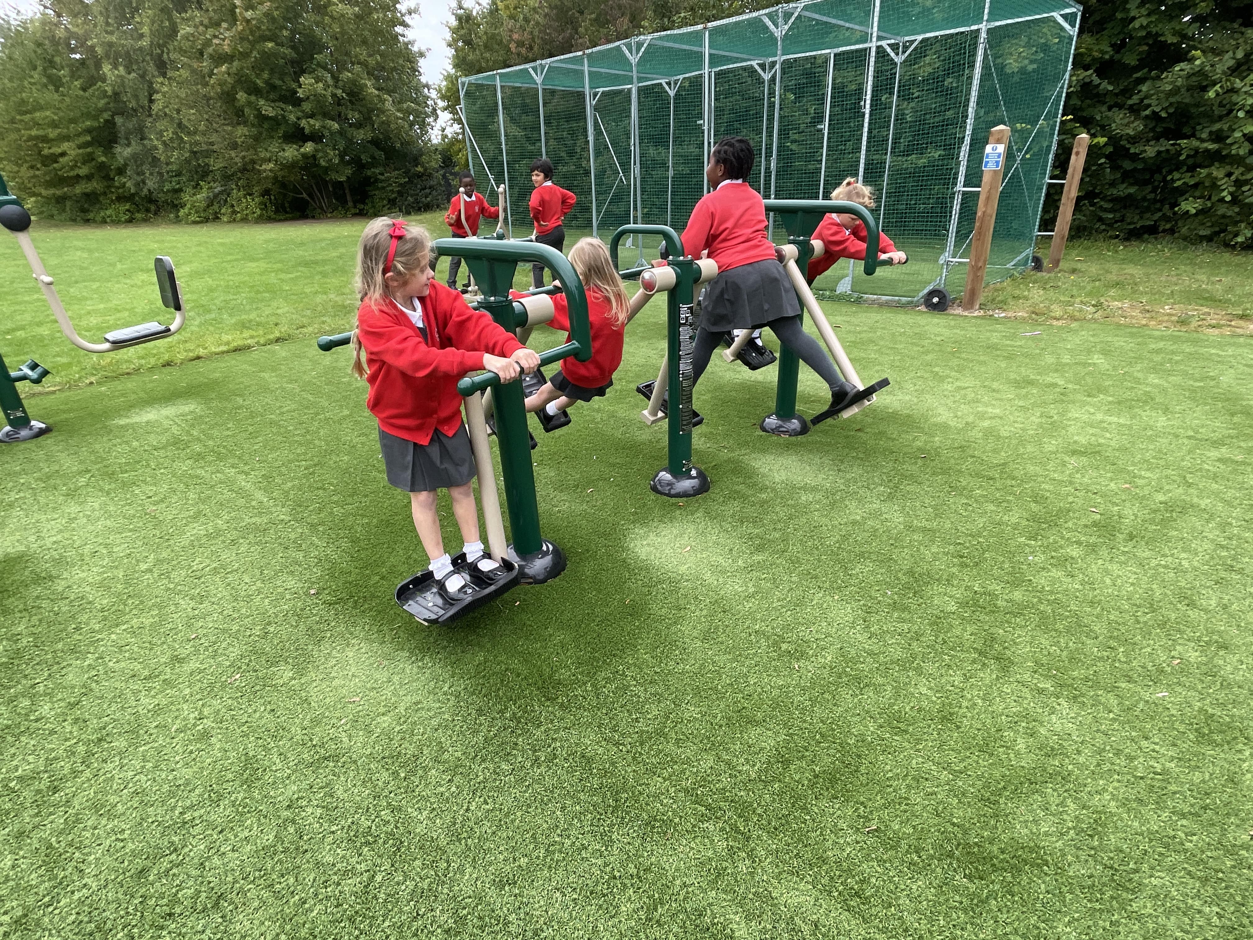 A group of children are playing on outdoor gym equipment, that's been installed on artificial grass.